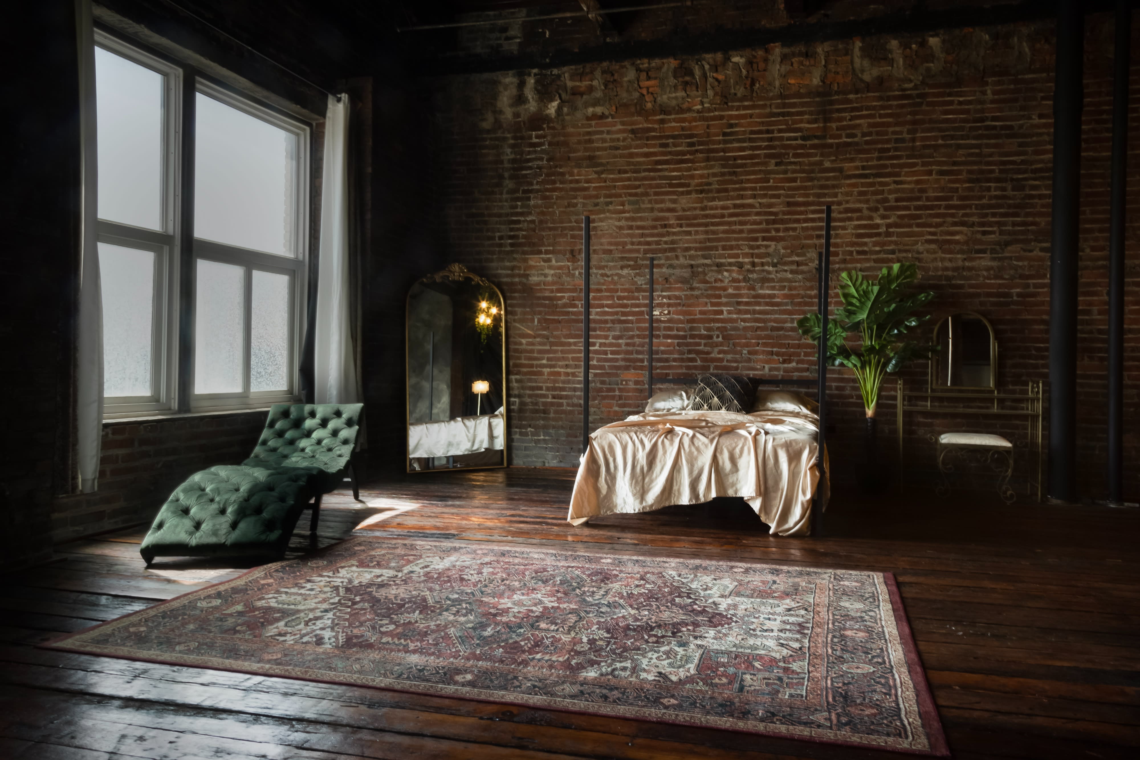 A woman in a flowing white dress poses gracefully in a softly lit, vintage-inspired room with exposed brick walls and elegant decor.