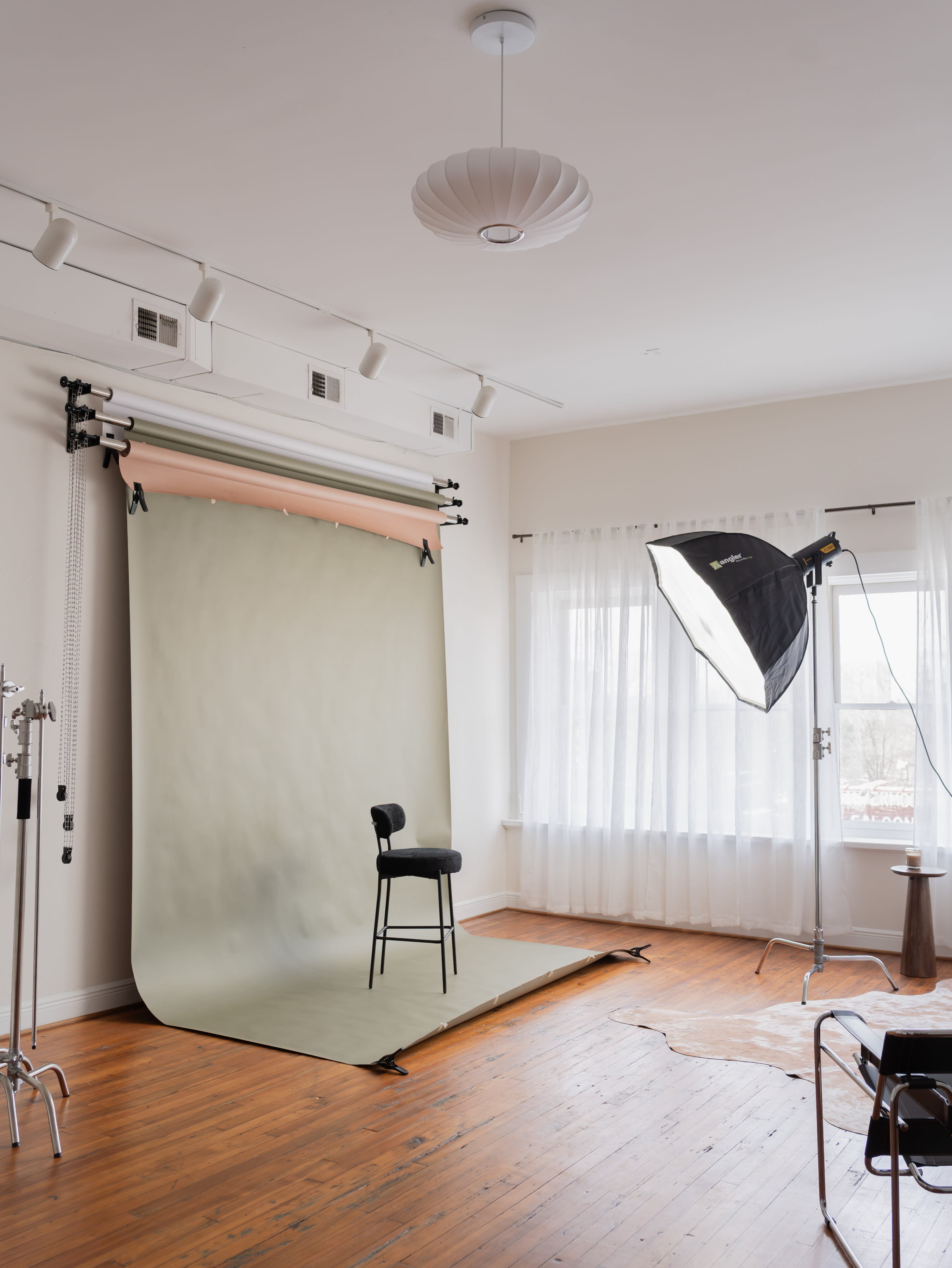 The scene depicts a bright studio with large windows, showcasing a cozy couch, and soft shadows cast by the sunlight filtering through sheer curtains.