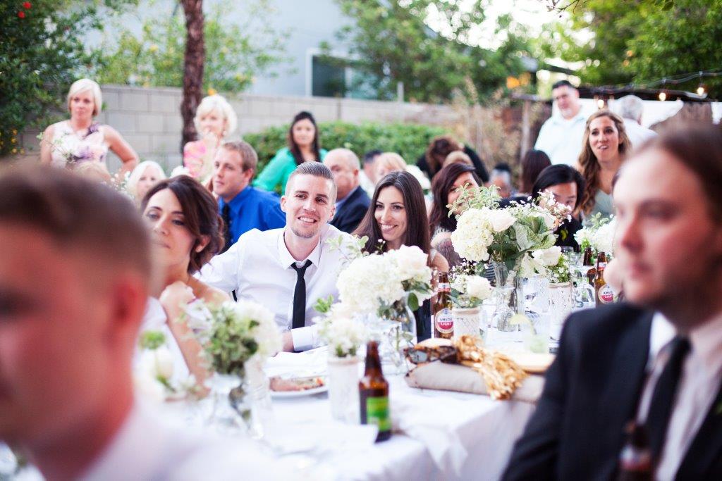 A bride in a white gown holds a floral bouquet and displays her ring in a garden setting decorated with lights.