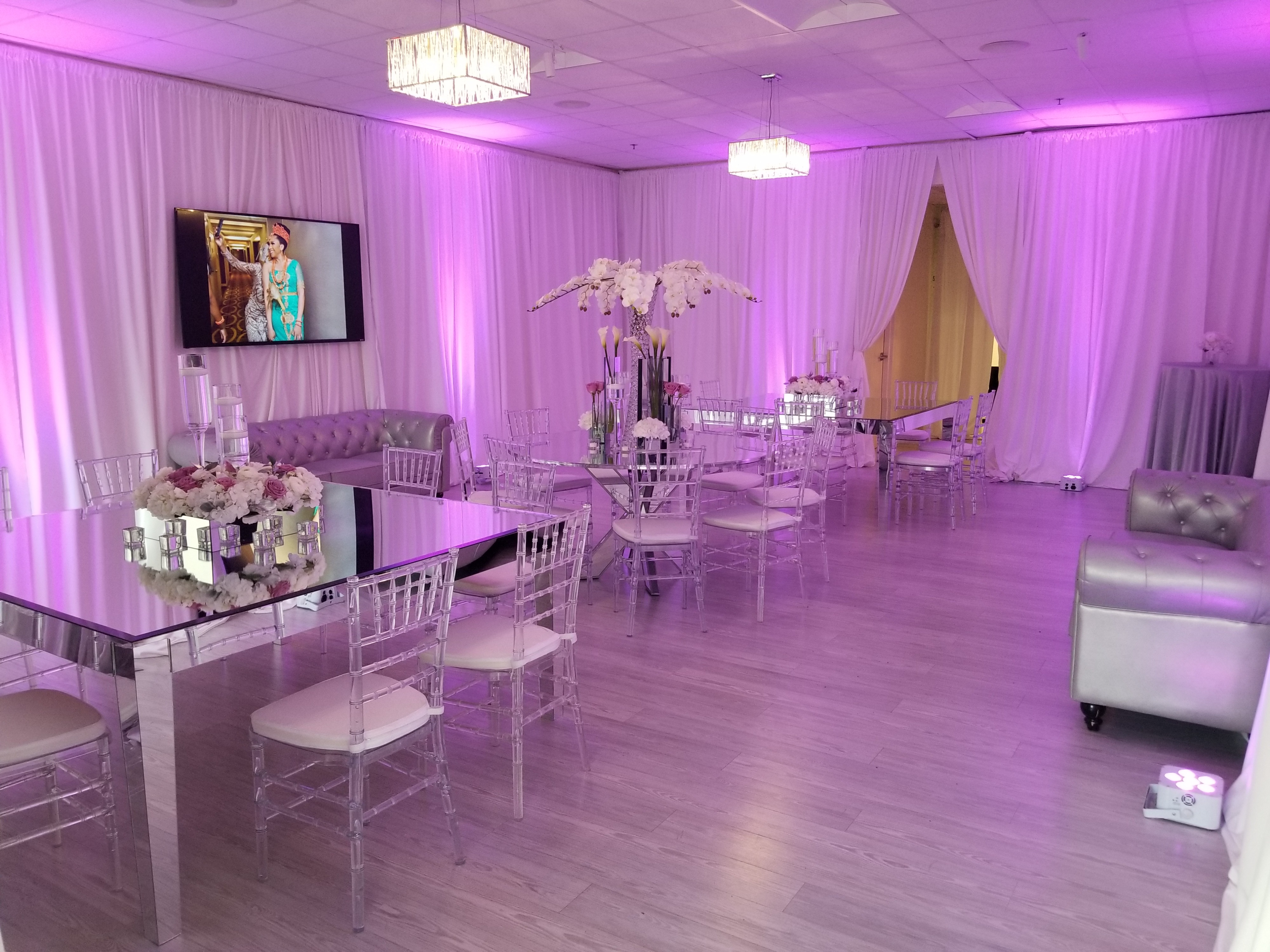 A decorated event space is set up for a baby shower, featuring gold chairs, elegant table settings, and greenery accents.