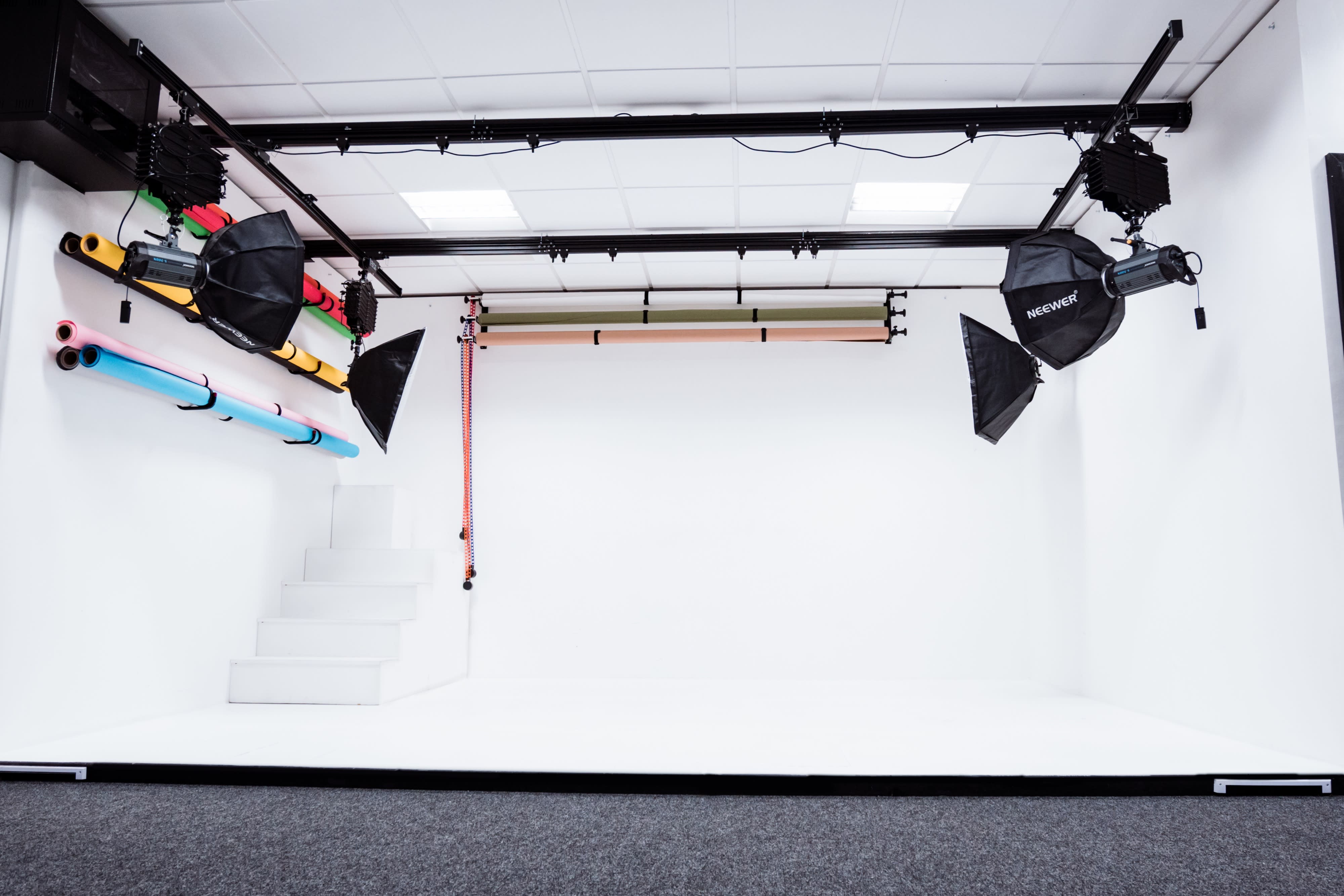 A blue suitcase is positioned in the center of a minimalist white studio, surrounded by black and colored lights and equipment.