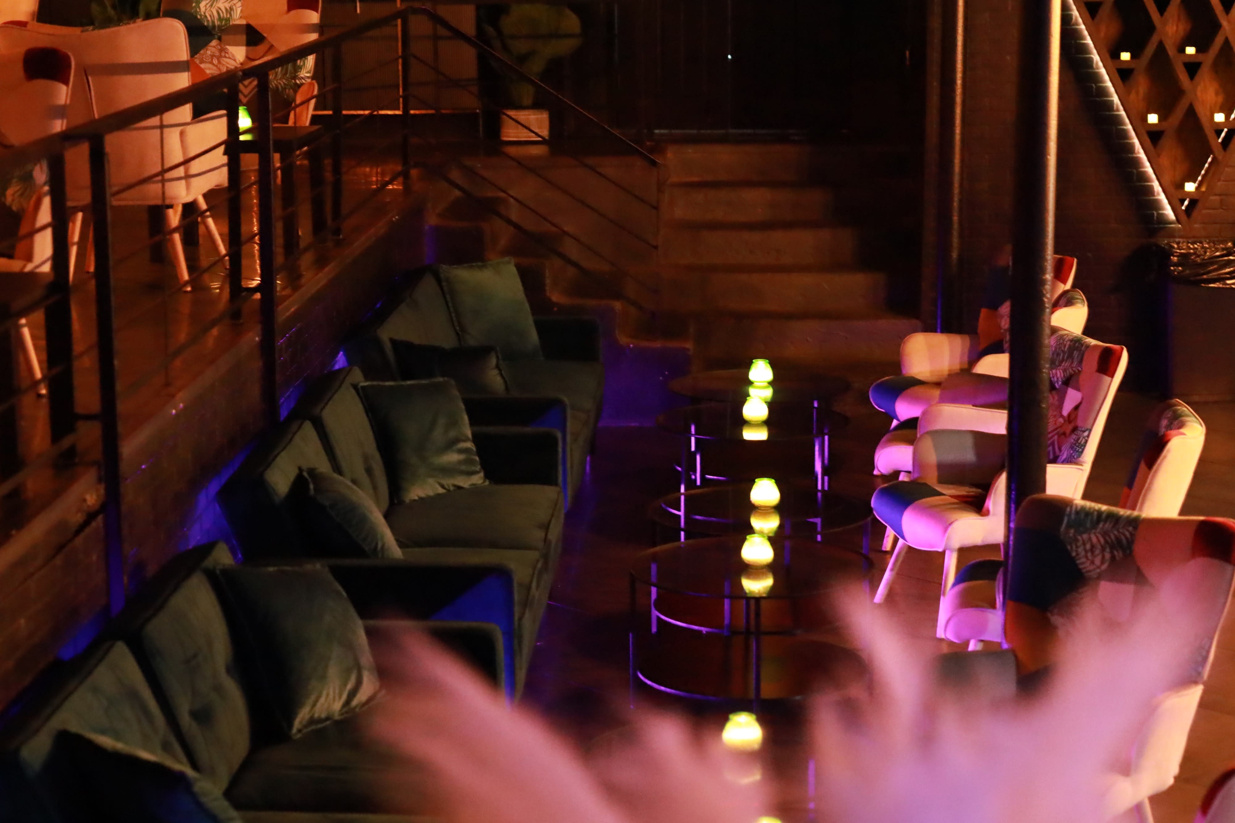 A photographer sets up a shot in a bar while a model poses on a stool, illuminated by a large umbrella light.