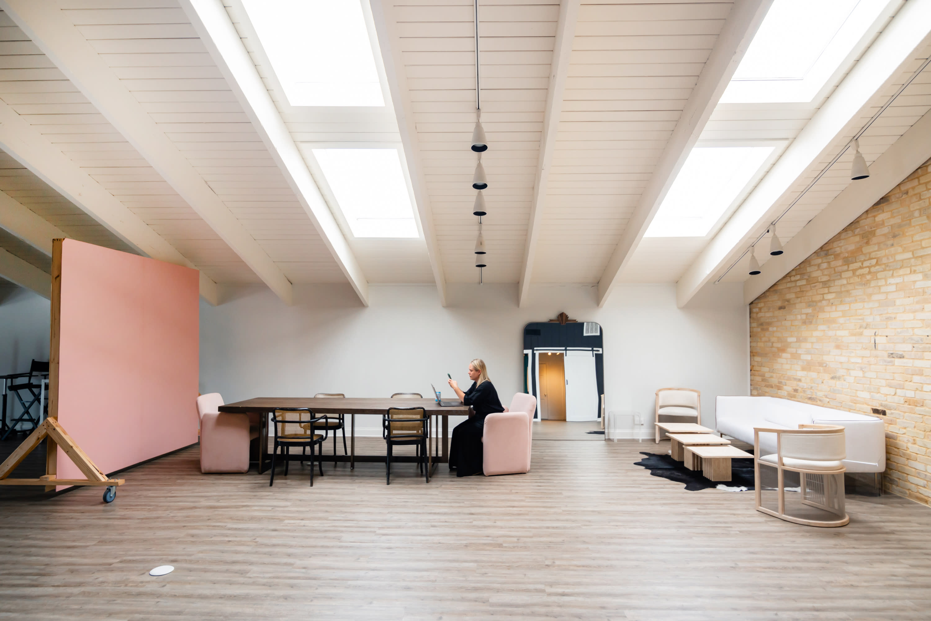 A photographer captures a seated model in a spacious studio featuring high ceilings and large windows.