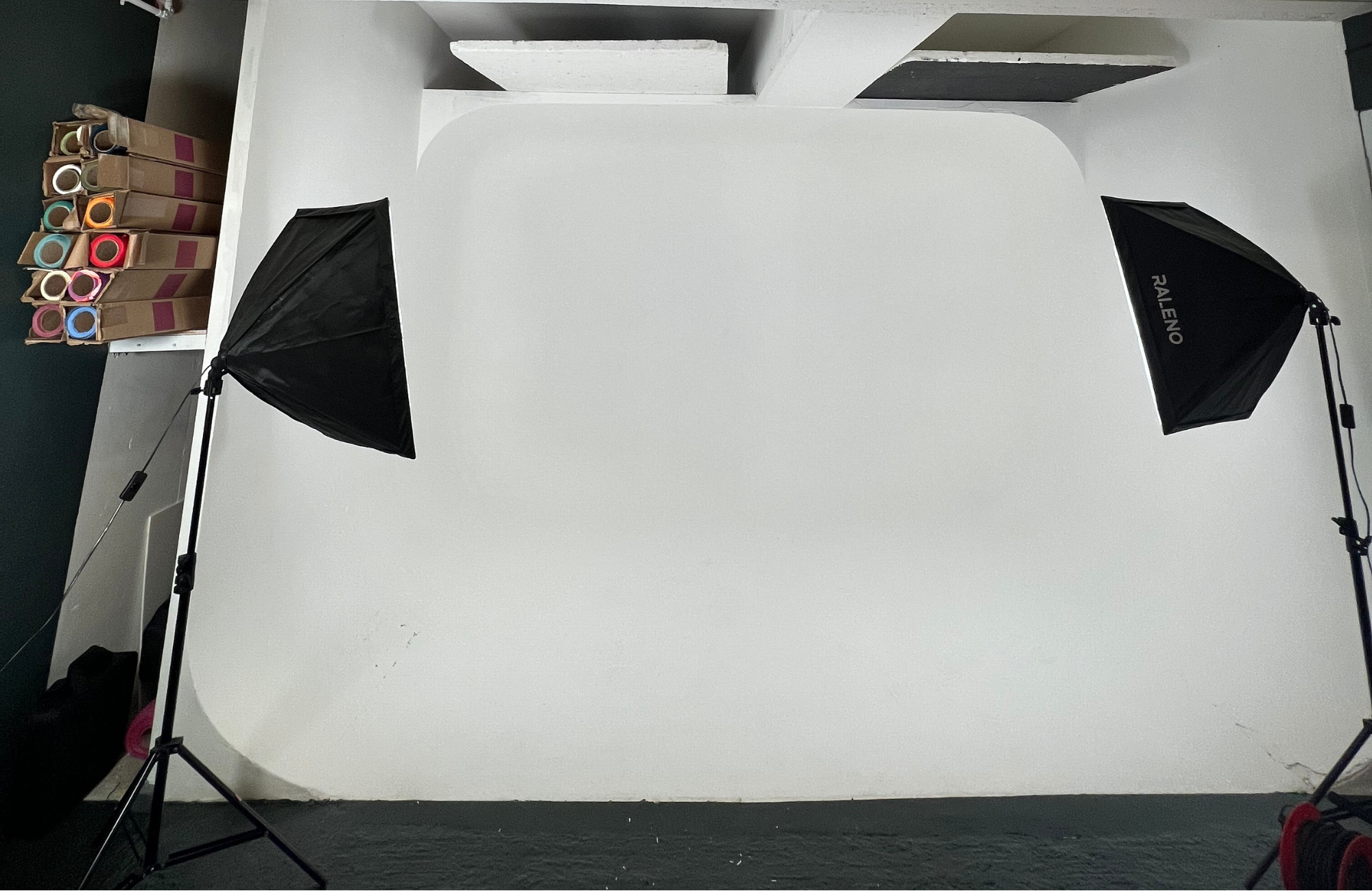 A model poses in a black outfit while a photographer adjusts lighting equipment in a studio.