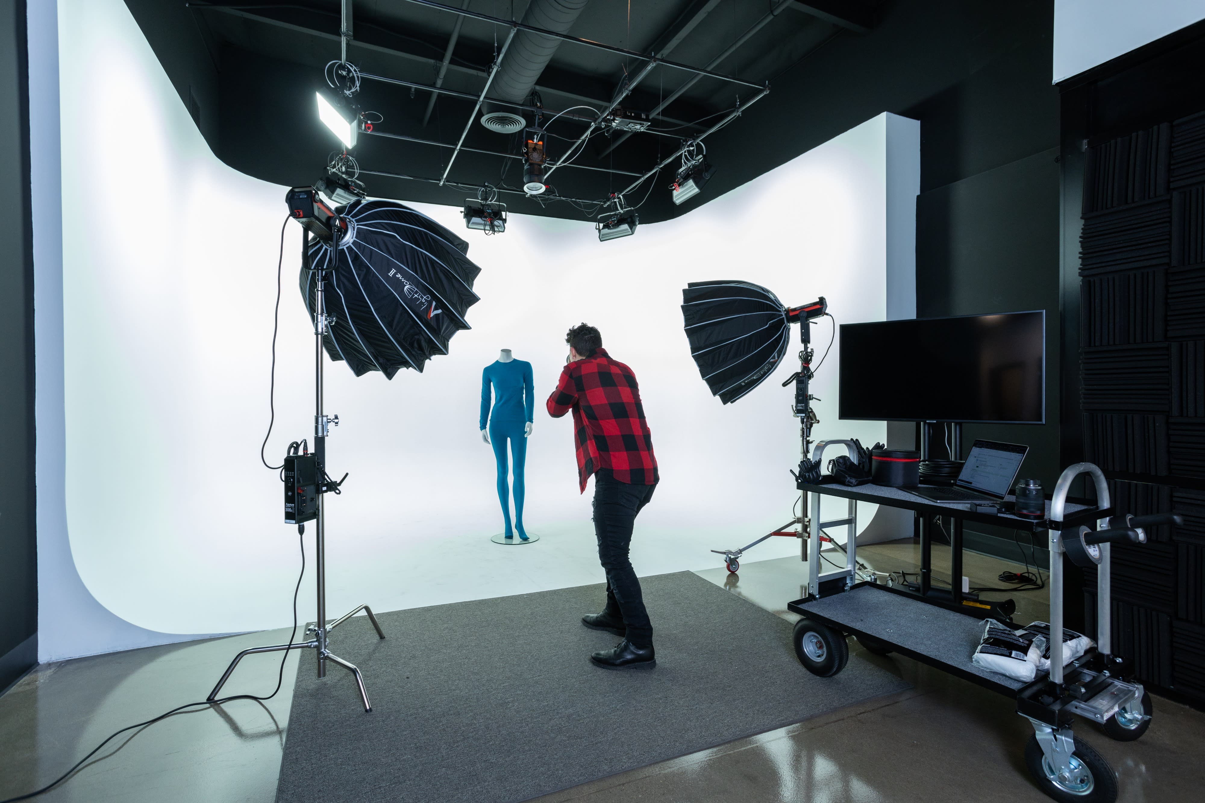 The scene features a video shoot setup with lighting umbrellas positioned in front of a colorful backdrop.