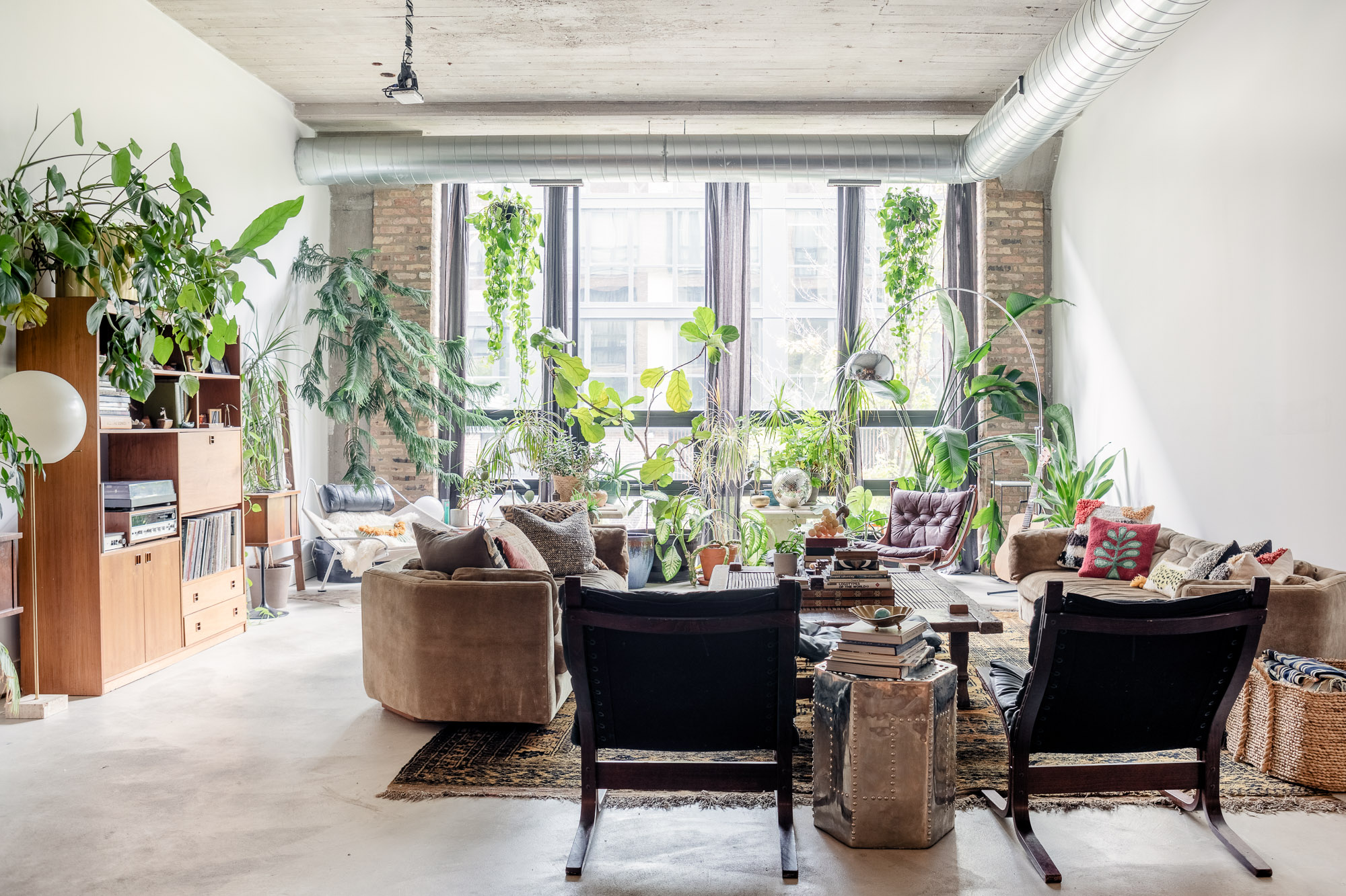 A group of people participates in a photography workshop in a cozy, plant-filled space, with one person posing for the camera while others offer guidance.