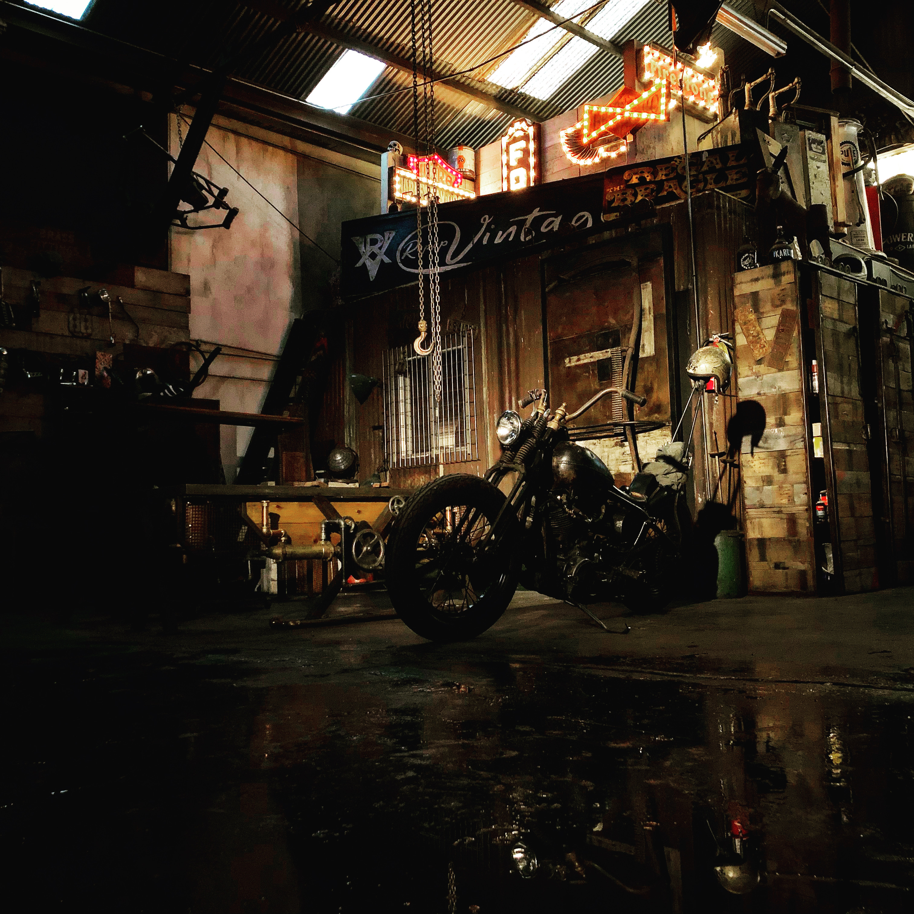 A man in shorts and sneakers poses on the hood of a bright green car in a dimly lit garage with casino-themed decor.