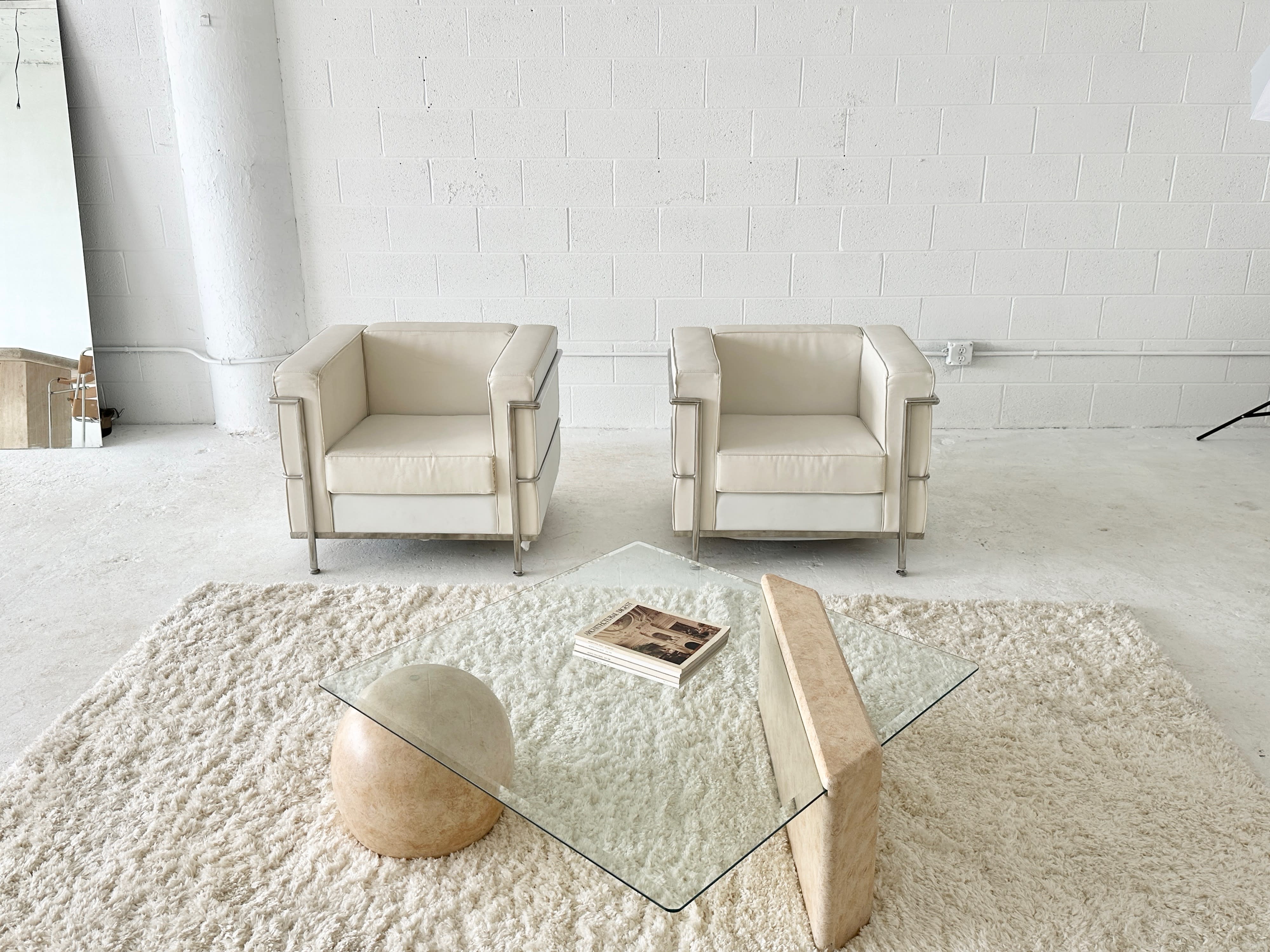 A woman in a blazer examines jewelry pieces displayed on a table while working on a laptop in a spacious, modern studio.