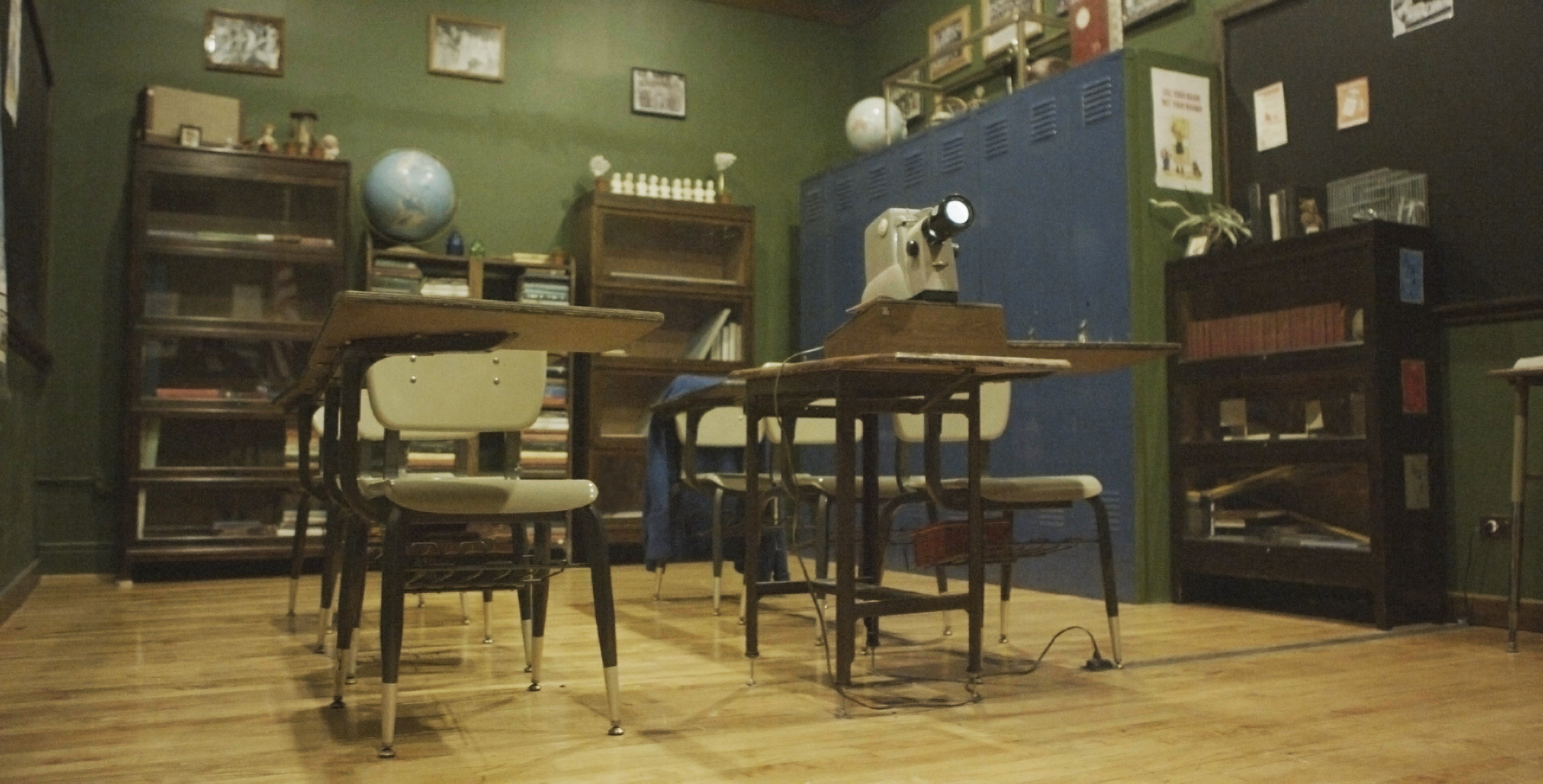 A group of six girls is seated at desks in a classroom setting as part of a warehouse music video shoot.