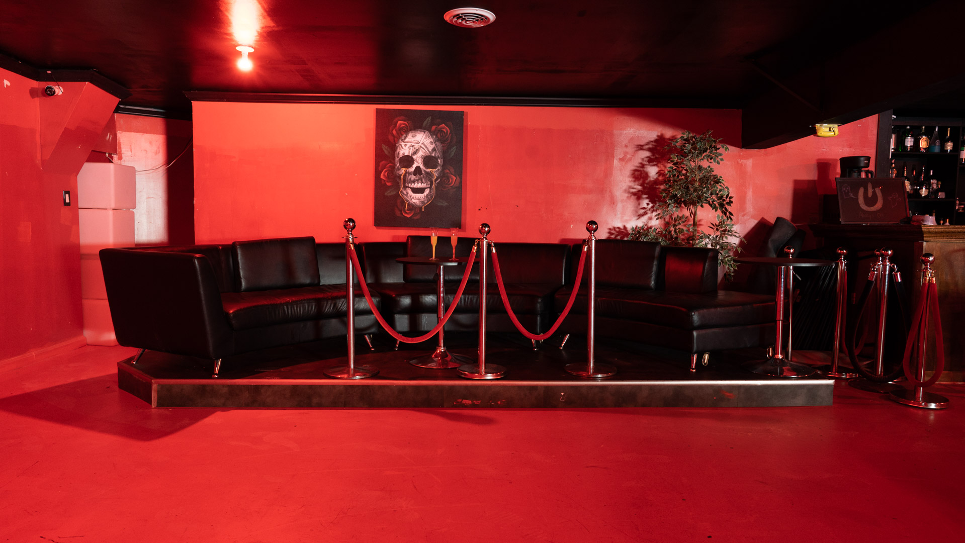 A group of people socializes and poses on red couches in a dimly lit room adorned with decorations and scattered money on the floor.