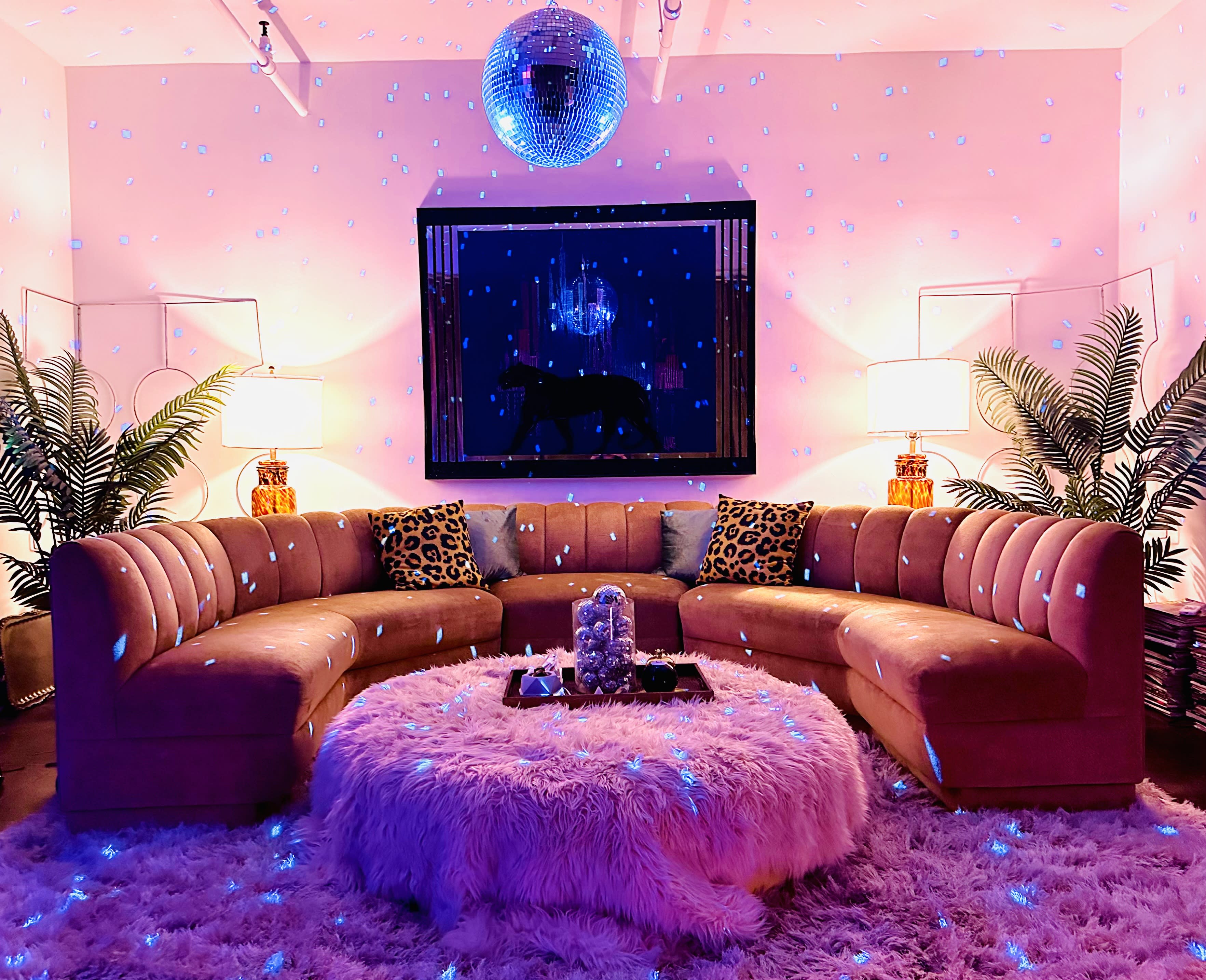 Three women are styled in vintage outfits and hair rollers, posed on a leopard-print bed while engaging in various activities like looking in mirrors, reading, and talking on a rotary phone.