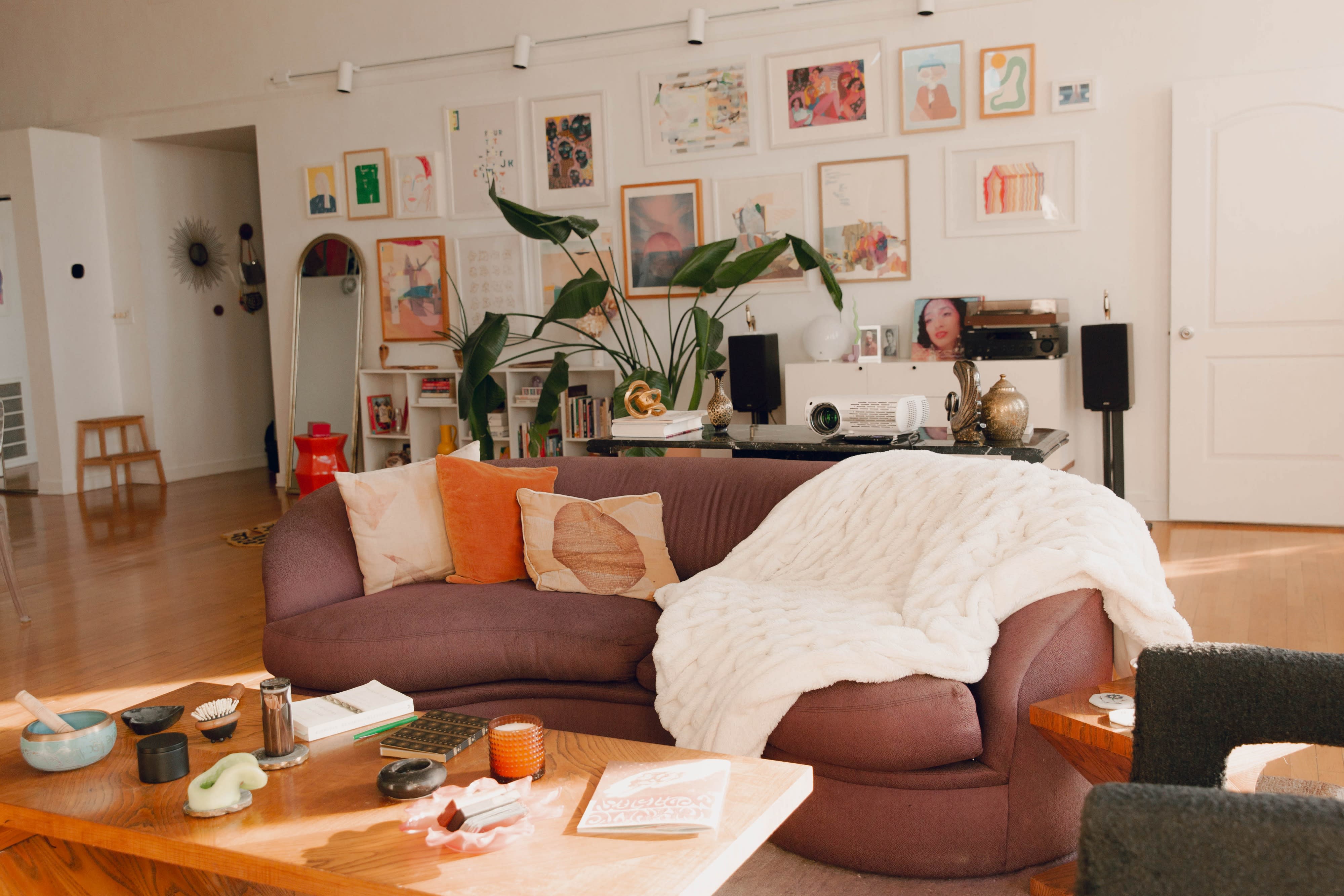 A model poses casually on a vibrant orange stool in a modern indoor space filled with framed artwork and greenery.