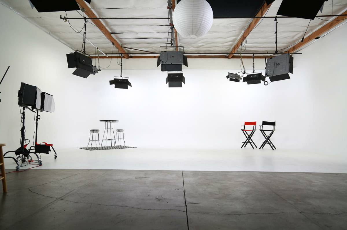 A dancer performs on a plain backdrop while being filmed by a camera setup on a tripod.