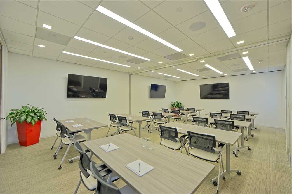 A group of participants engages in a workshop, actively discussing prompts displayed on a screen while seated at tables with materials and water bottles.