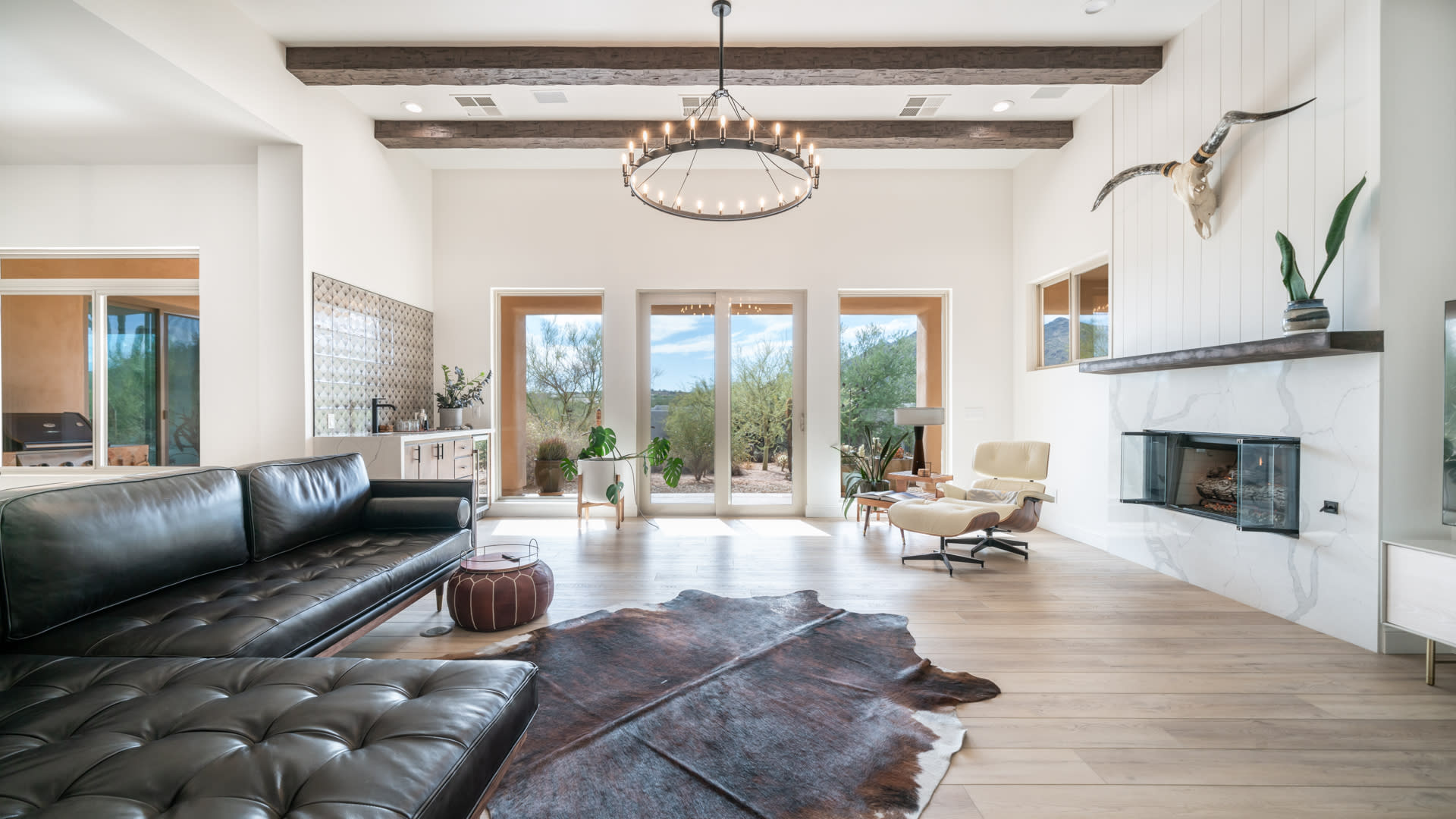 A filmmaker sets up equipment for a documentary shoot in a spacious, sunlit living room with large windows overlooking a landscape.