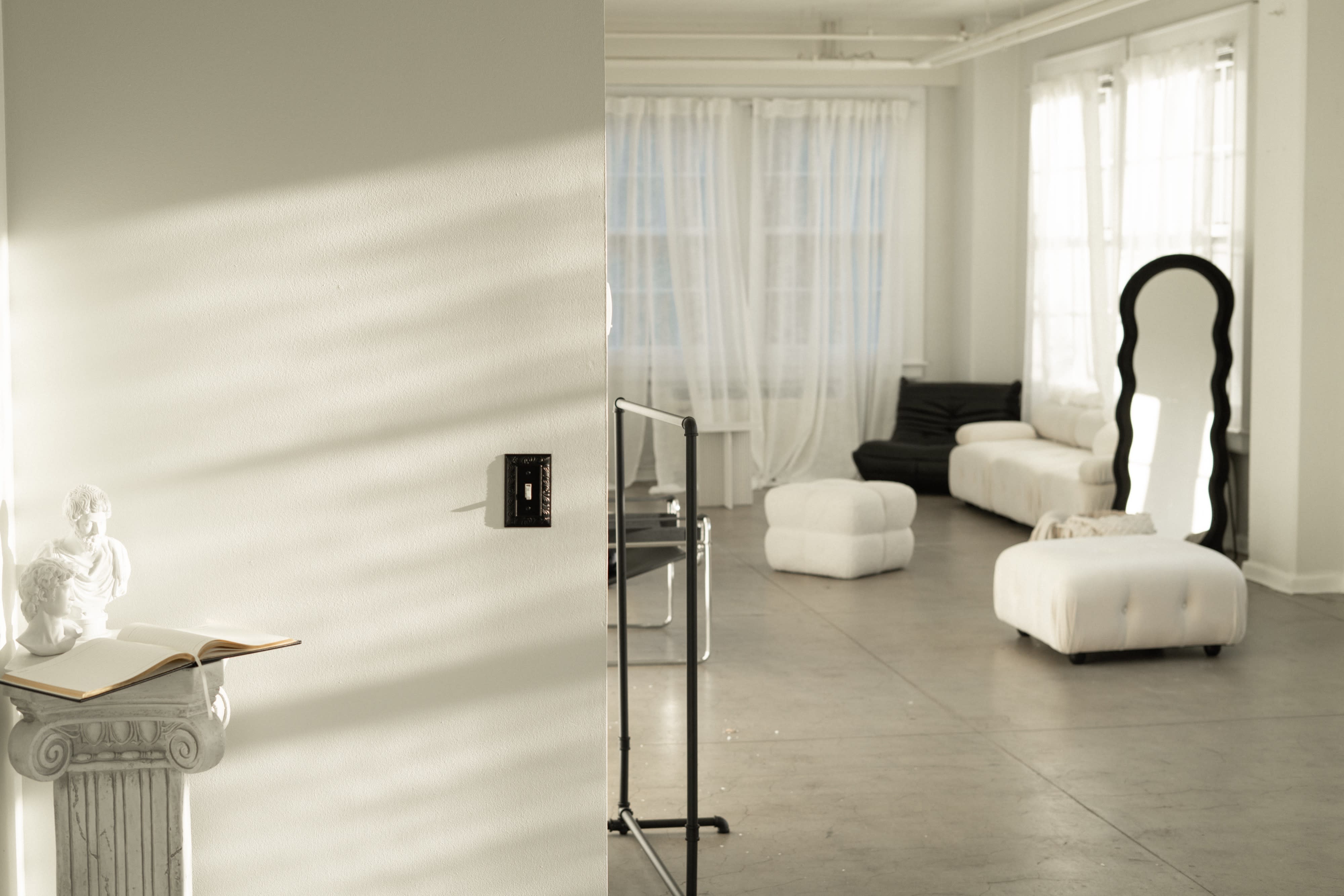 A model poses thoughtfully in a minimalist room, seated on a sleek chair with a modern lamp in the background.