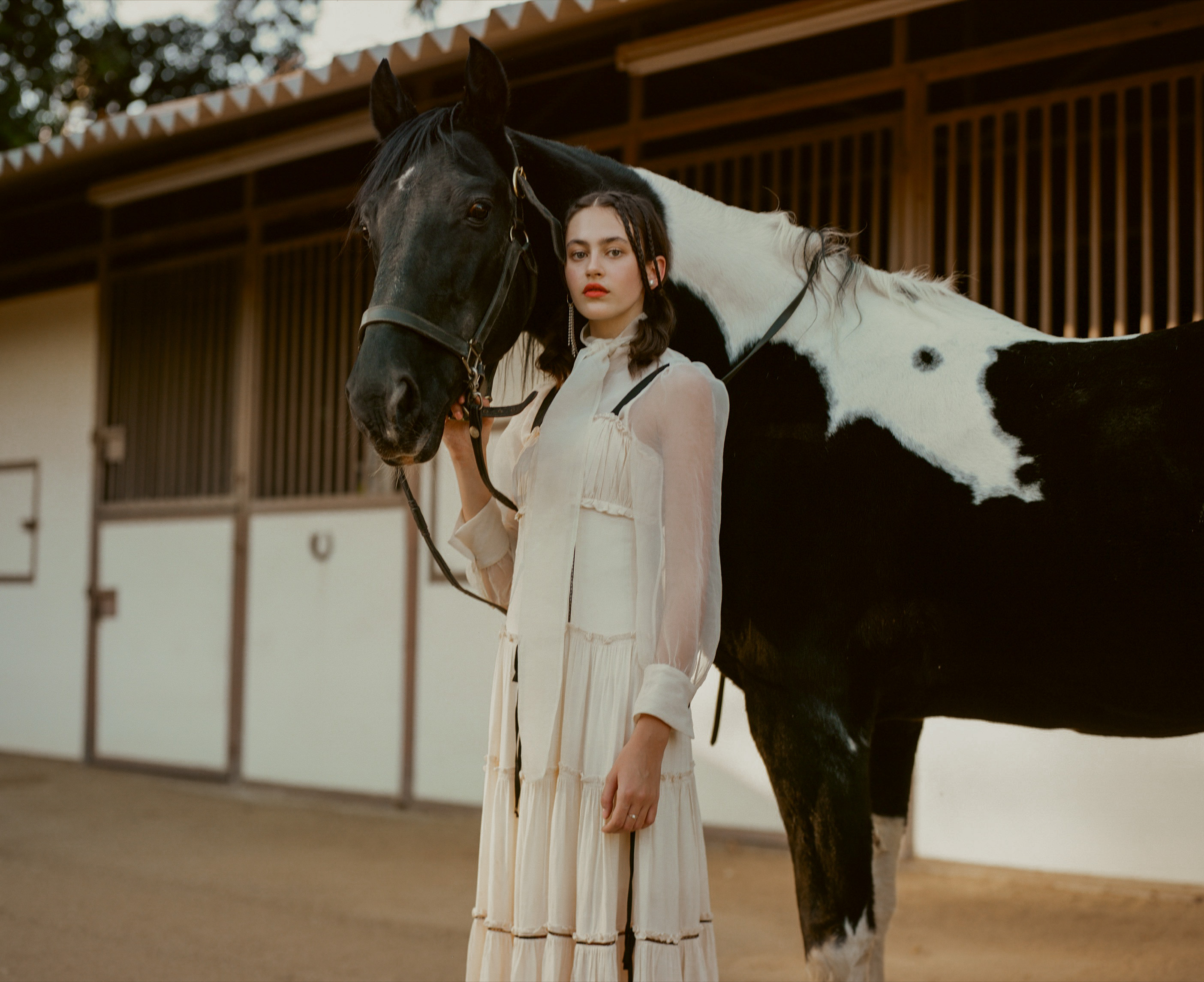 A couple poses for their engagement photo shoot in a rustic outdoor setting with a horse in the background.