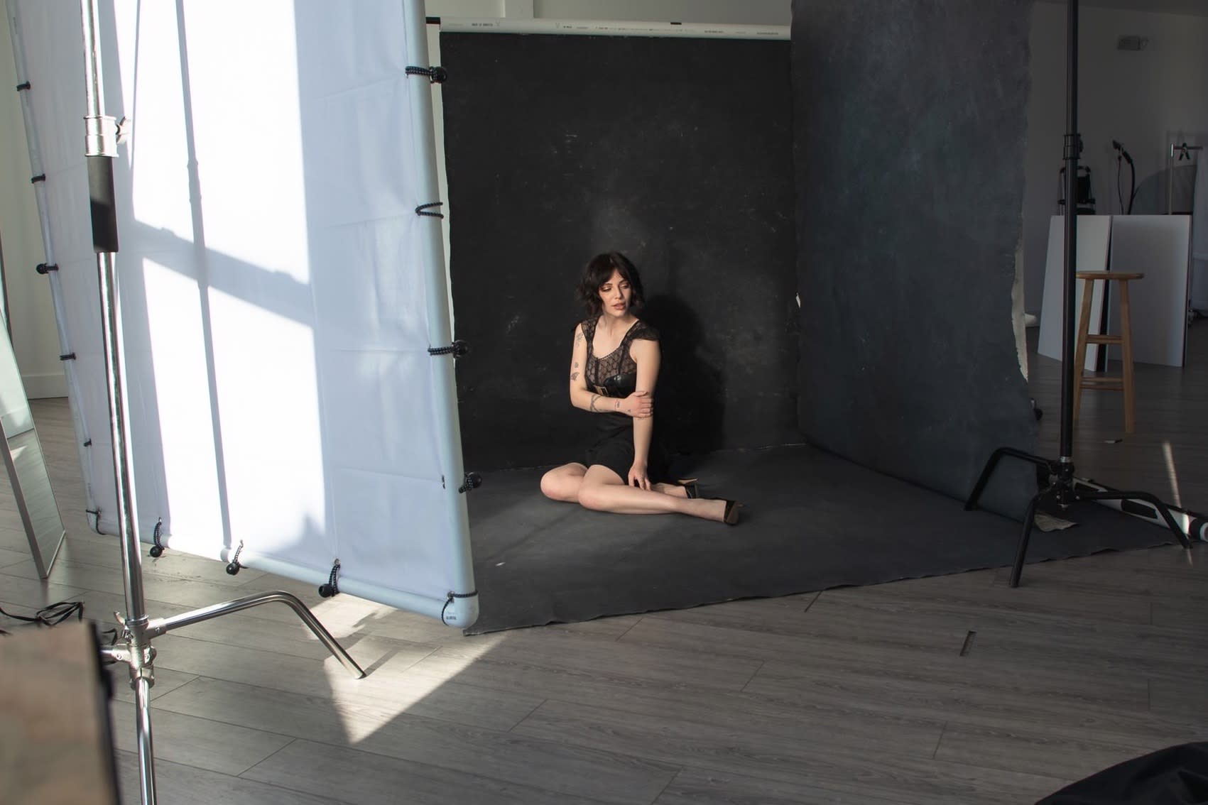 A model poses casually on a chair in front of a yellow backdrop and cacti during a photoshoot.