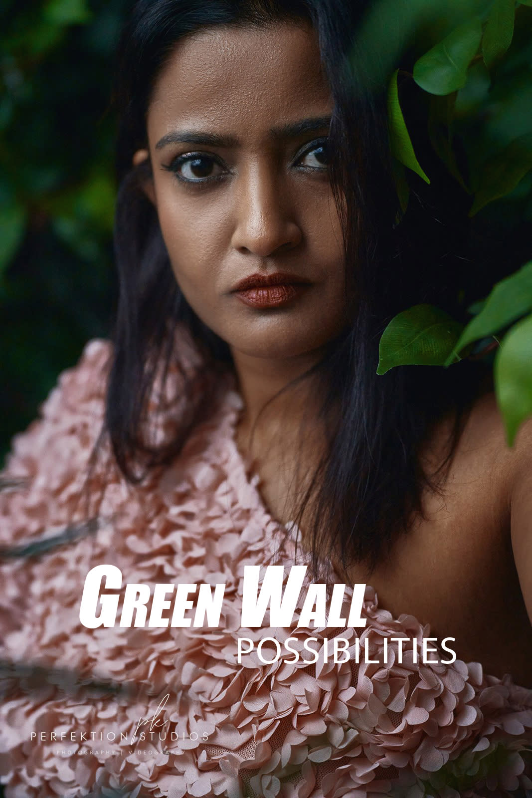 A photographer captures two women posing on a sofa in a studio adorned with greenery.