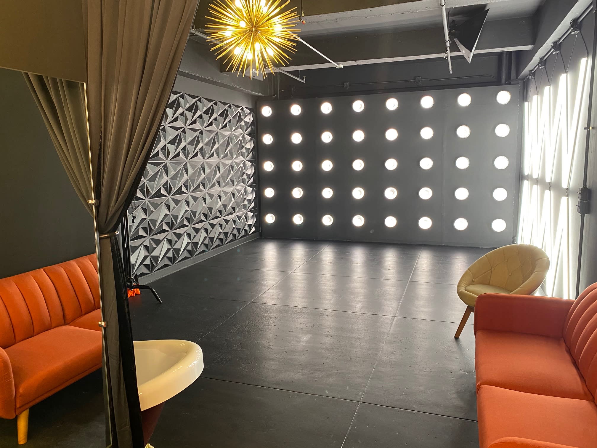 A person in a checkered outfit poses for a selfie in a room set up for a video shoot, with bright lights and crew visible in the background.