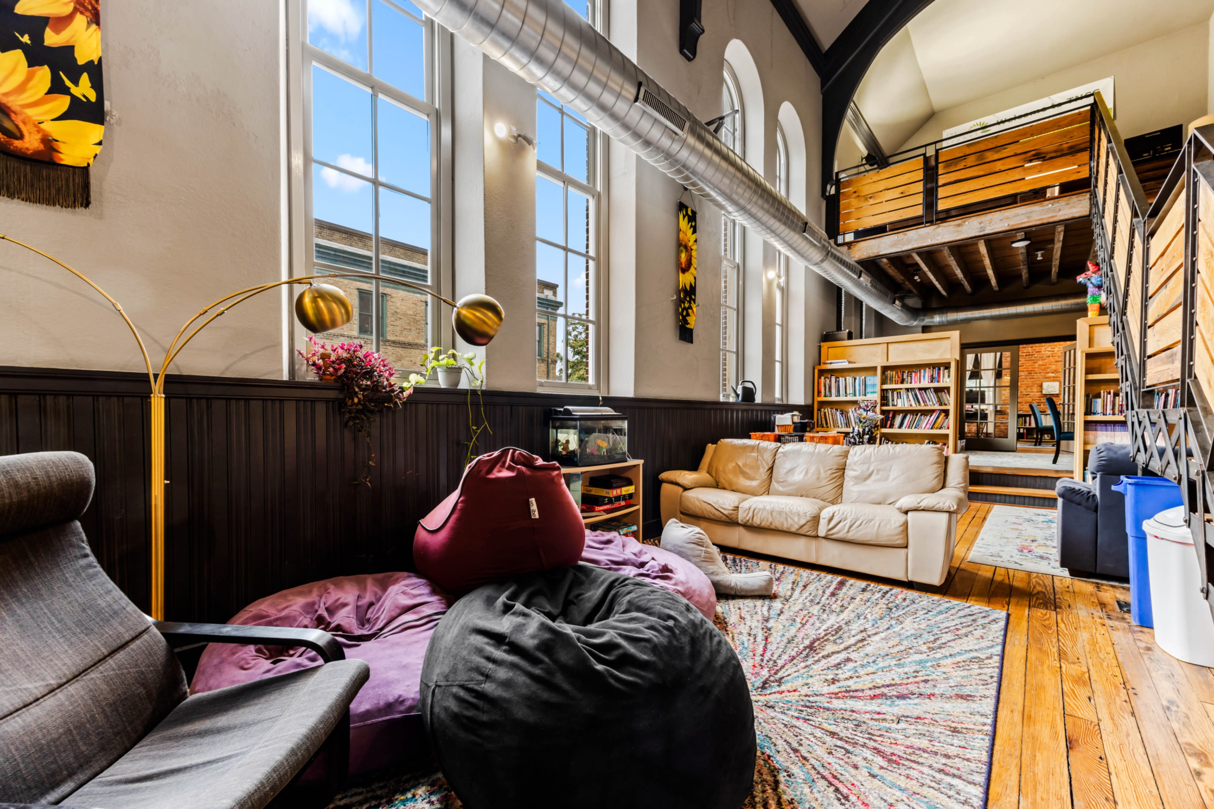 A group of people socializes and interacts at a cast party in a cozy, well-lit space adorned with bookshelves and large windows.