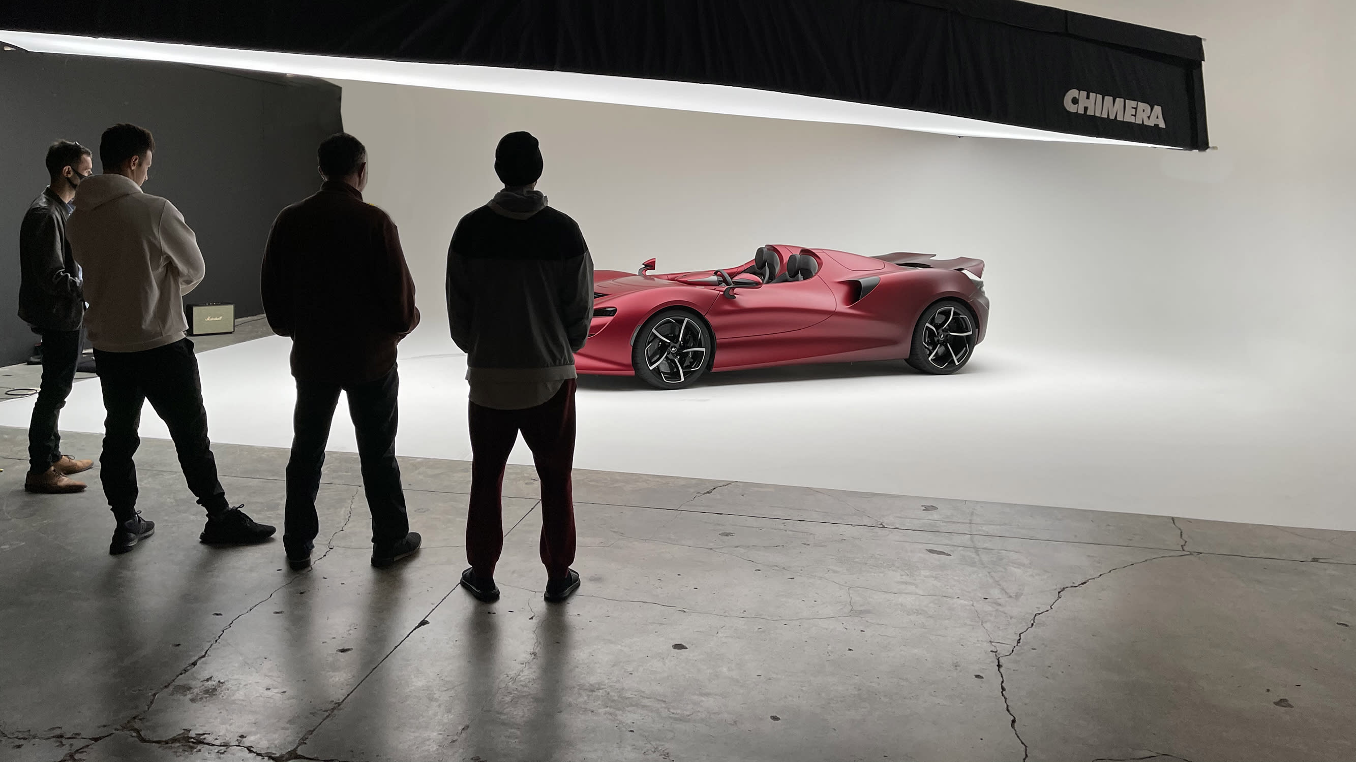 A team sets up camera equipment and lighting for a video shoot featuring a green vehicle on a studio backdrop.