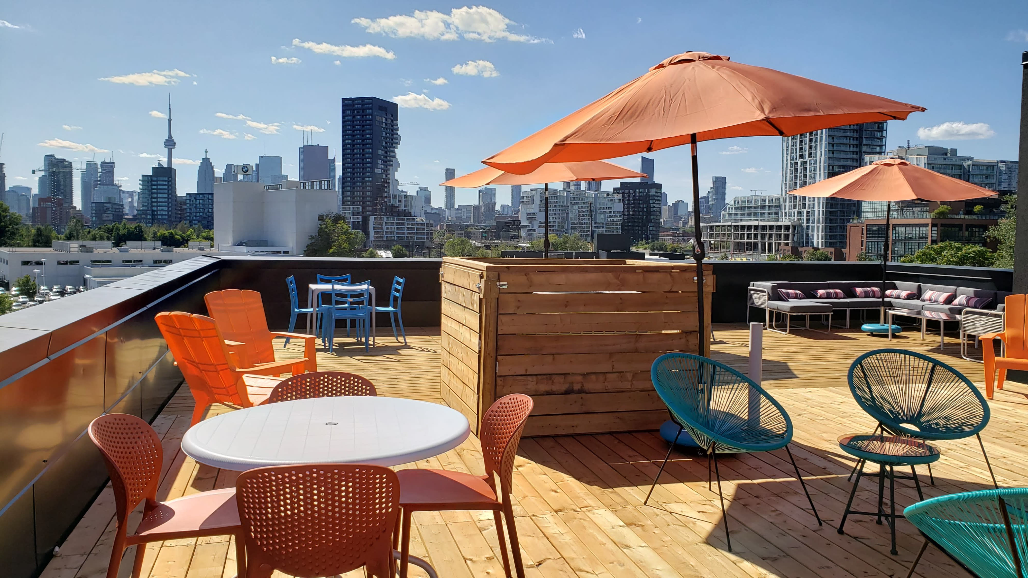 A group of people enjoy a birthday party on a rooftop terrace with food and drinks, illuminated by string lights at sunset.