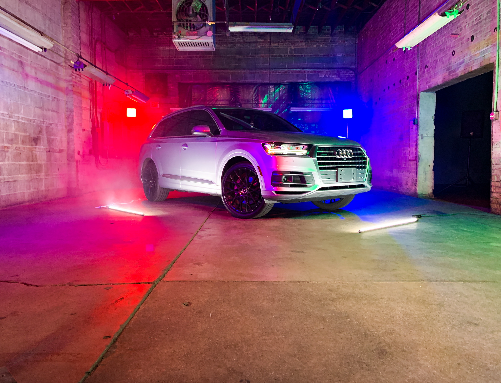 A crew films a video shoot featuring a vehicle in a dimly lit, misty setting with dramatic lighting.