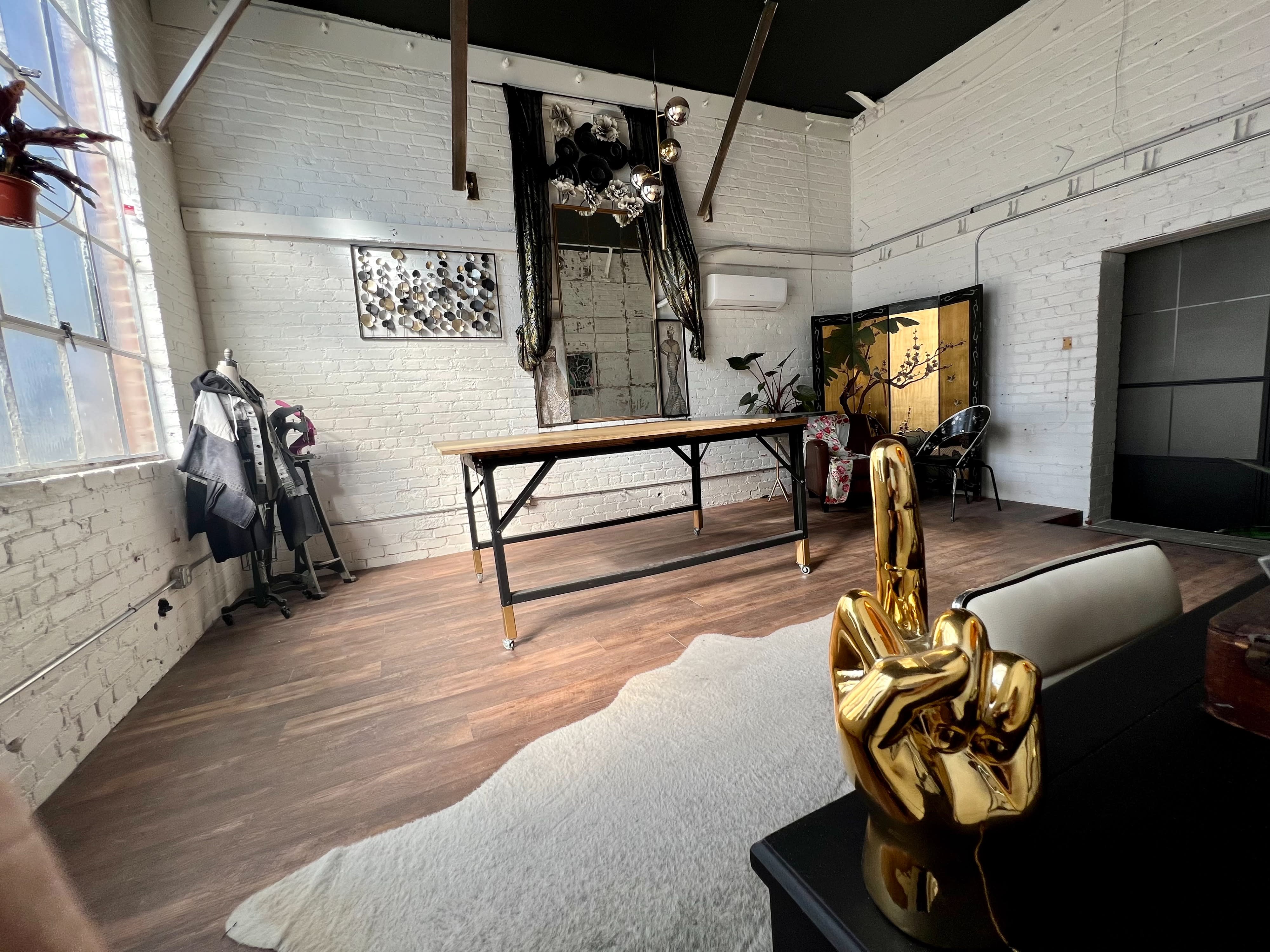 A spacious photo shoot studio features large windows, a stylish orange couch, a black chair, and a table with various items on it.