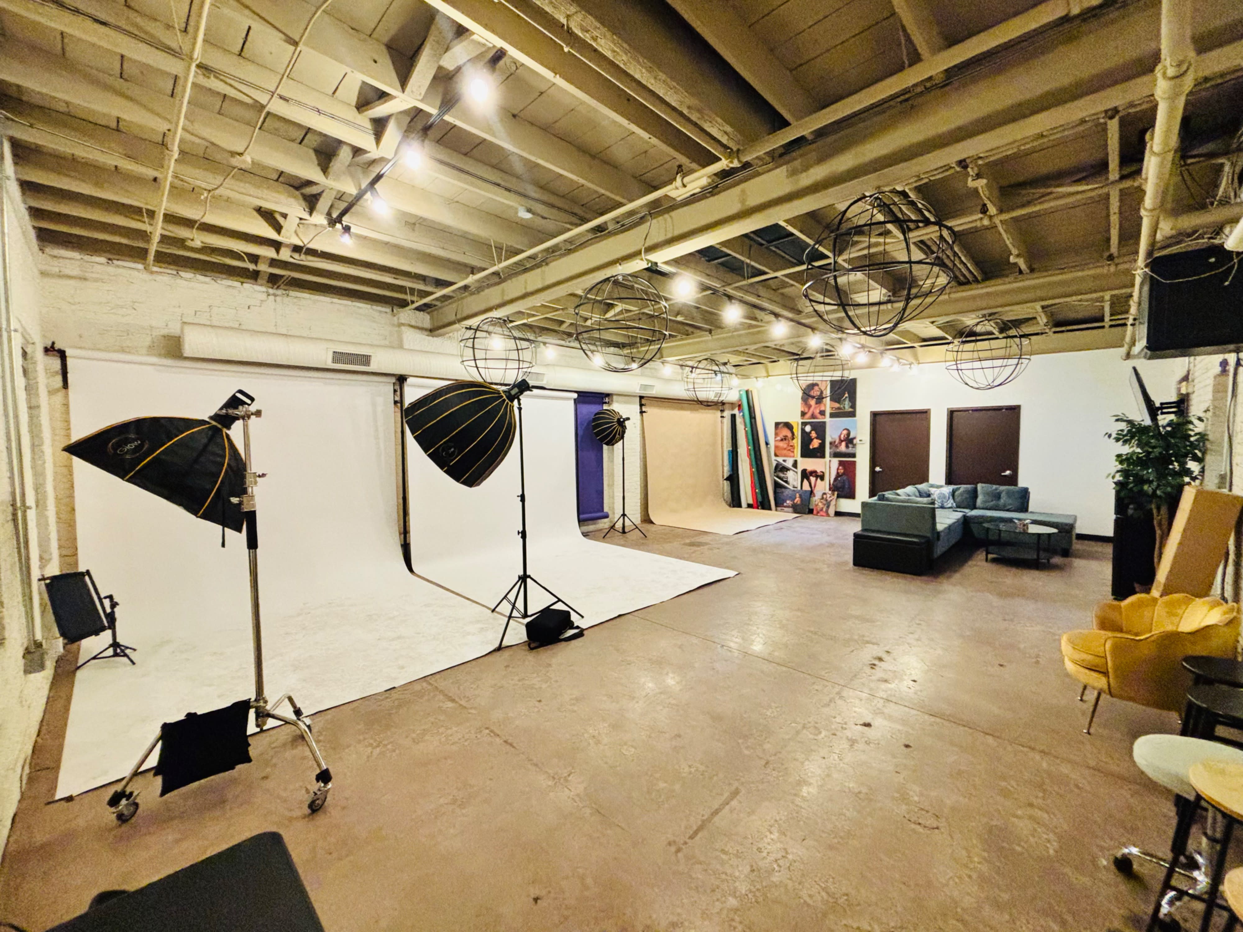 A model is getting her makeup applied by a stylist while a photographer adjusts equipment in a well-lit studio setting.