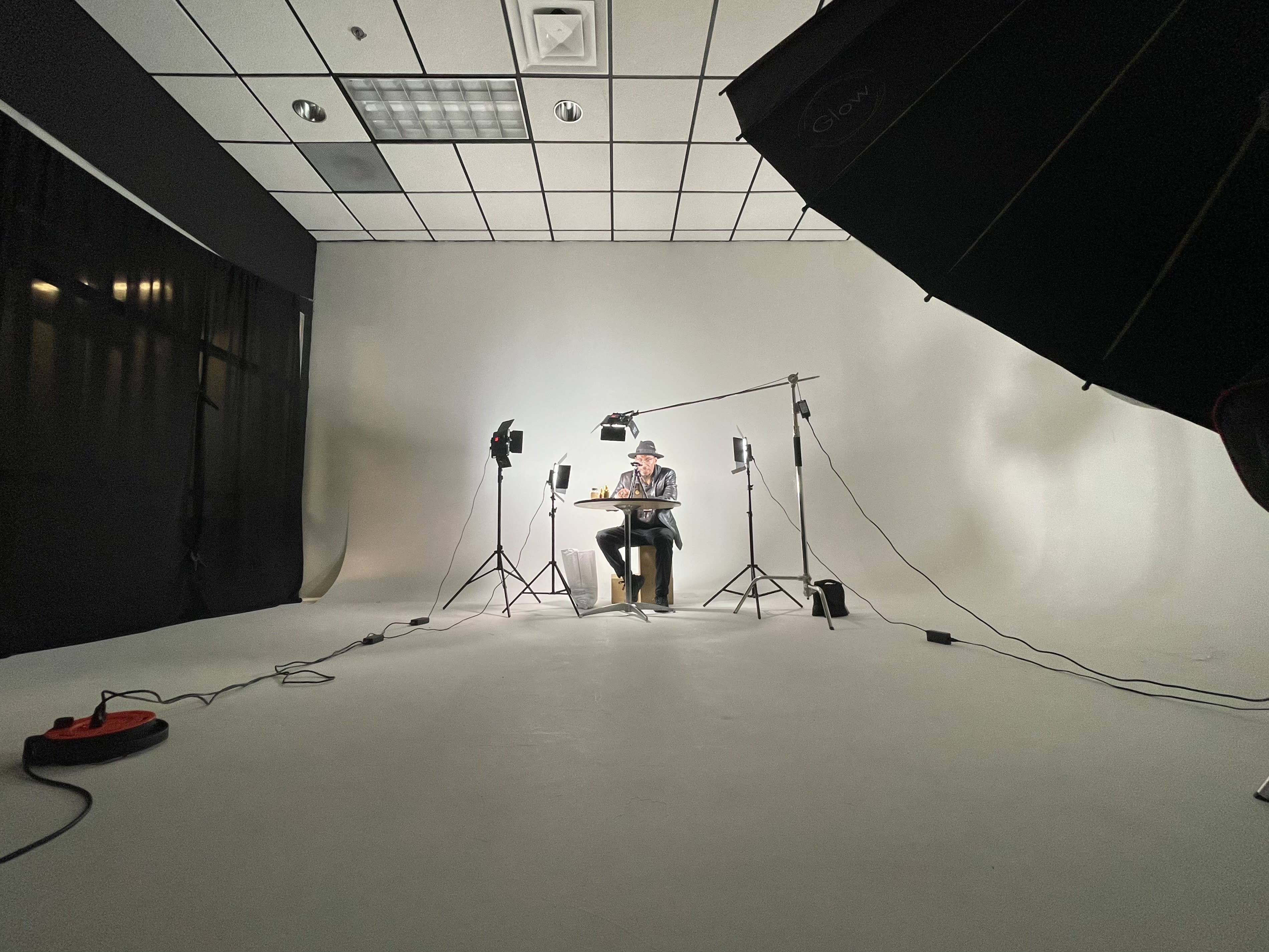 A person sits on the ground surrounded by scattered dollar bills while holding stacks of money in their hands during a photoshoot.