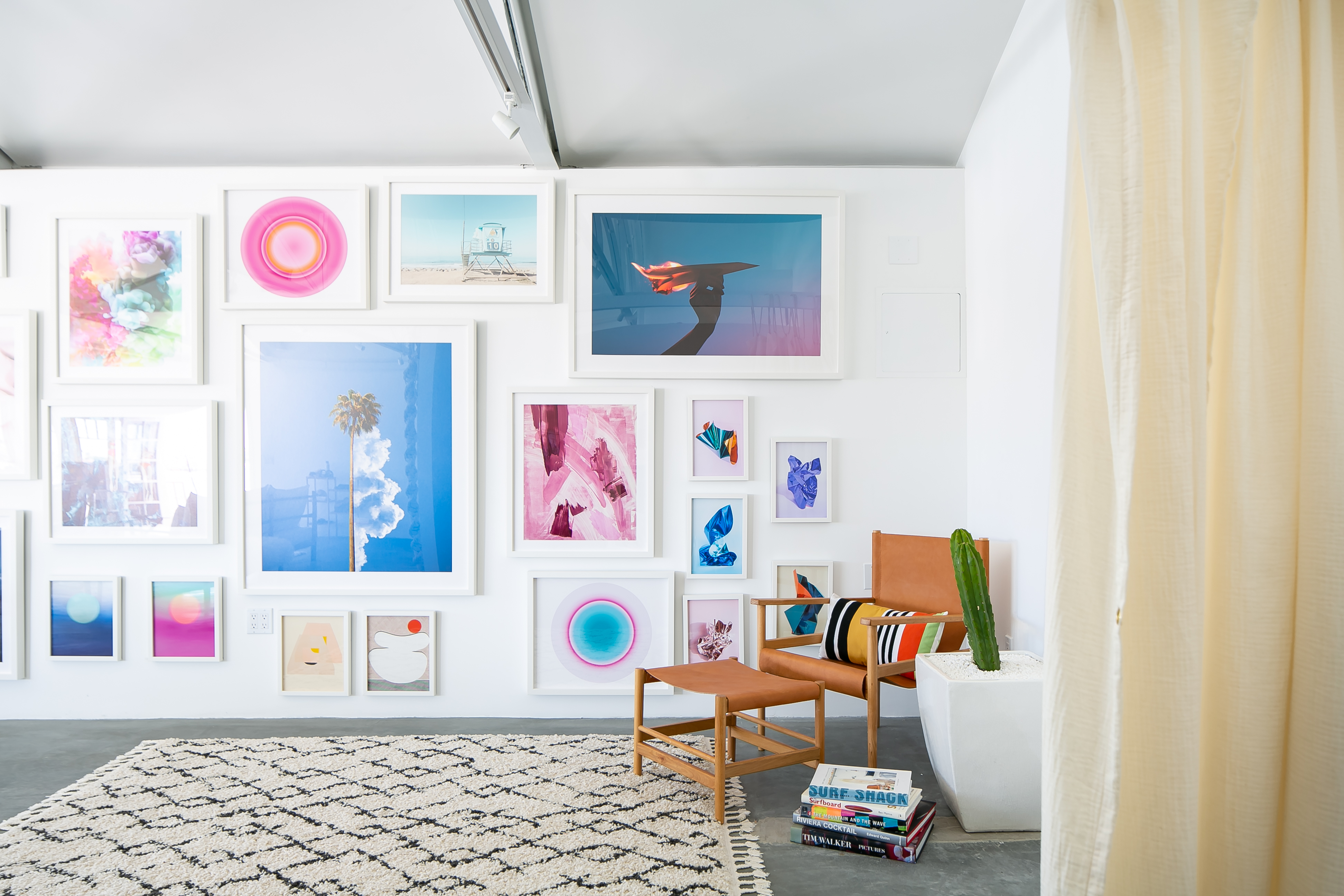 A spacious, well-lit studio features a wooden table, white sofas, and a wall adorned with framed artwork, ideal for a photoshoot.
