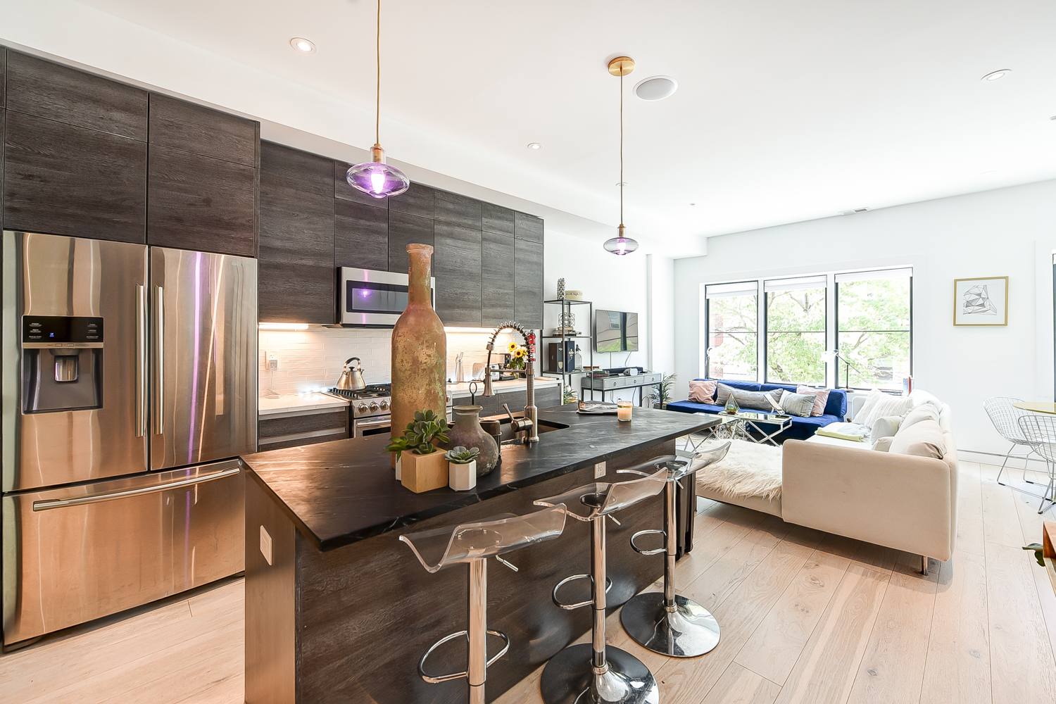 A model poses confidently on a kitchen countertop during a photoshoot, showcasing her outfit and the modern kitchen setting.