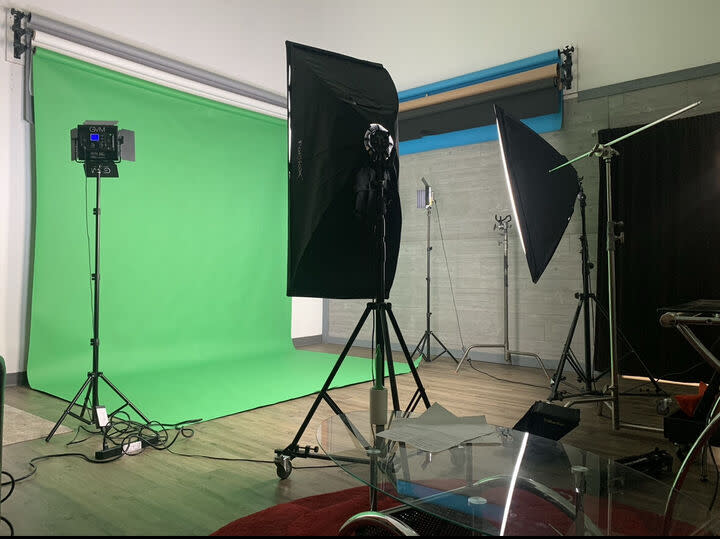 A person in scrubs stands in front of a green screen setup for a video shoot.