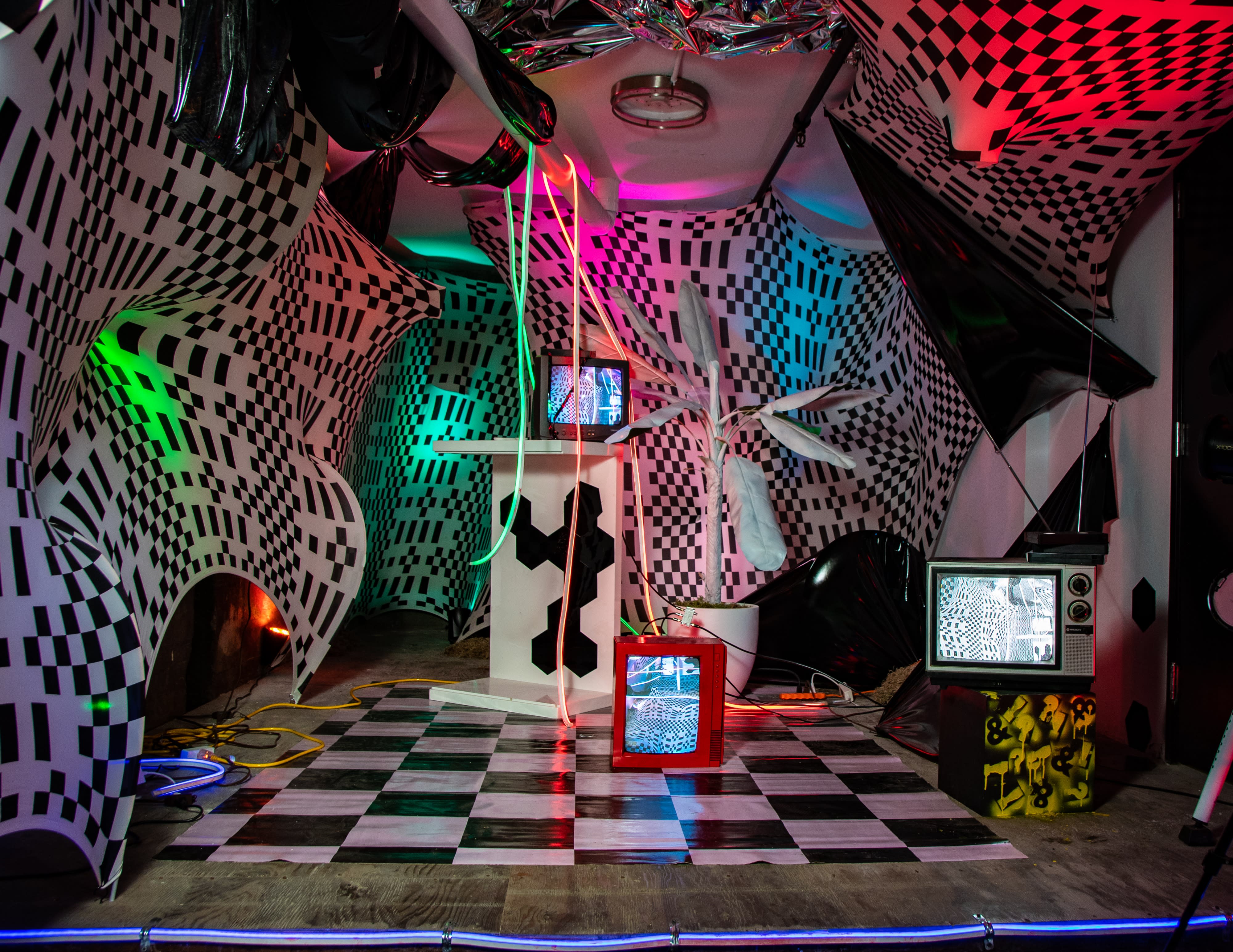 A model poses on hands and knees in a reflective, mirrored environment, showcasing vibrant nail art.