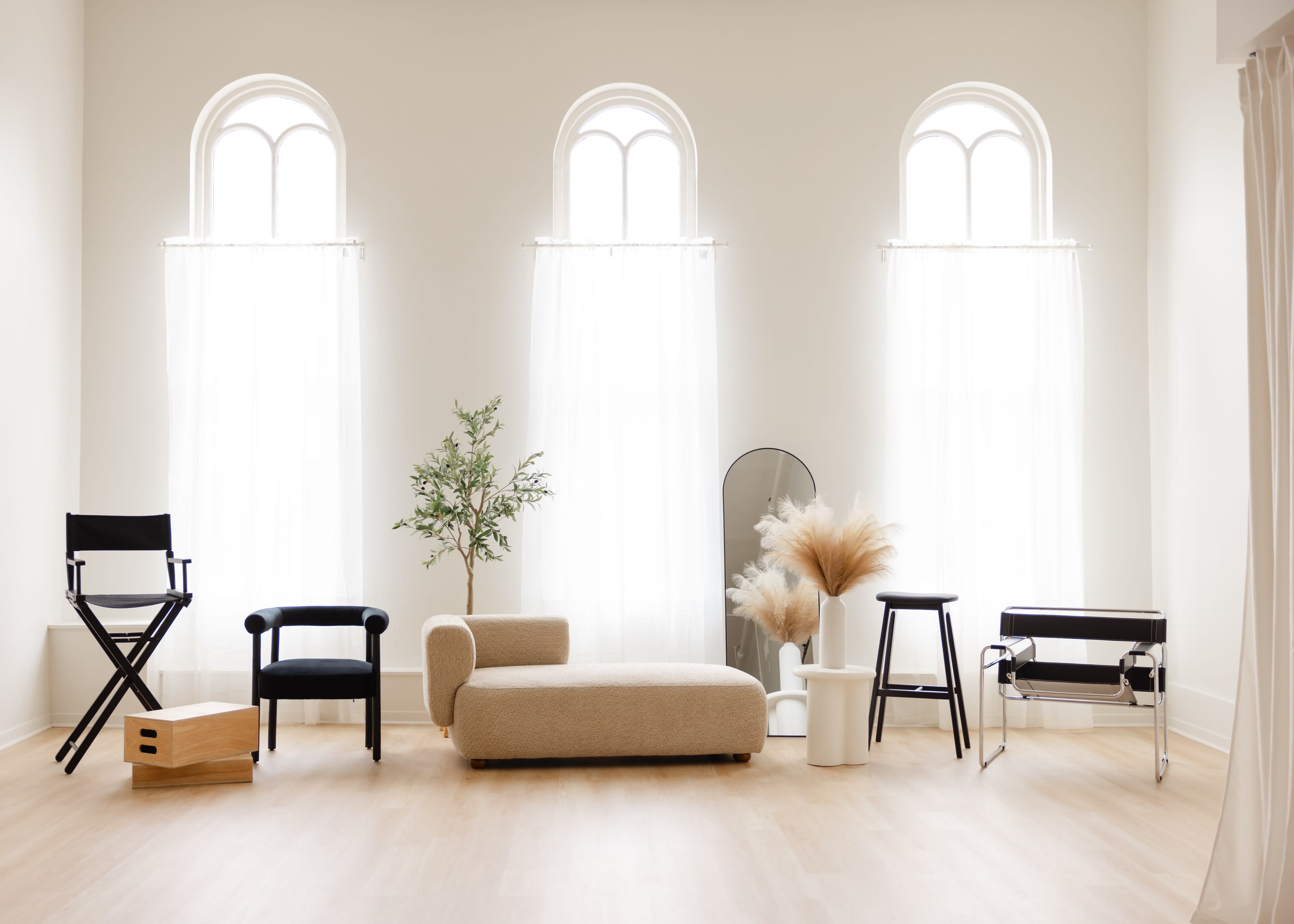A bright, spacious photoshoot studio features a clean, white backdrop, natural light streaming through large windows, and textured walls.