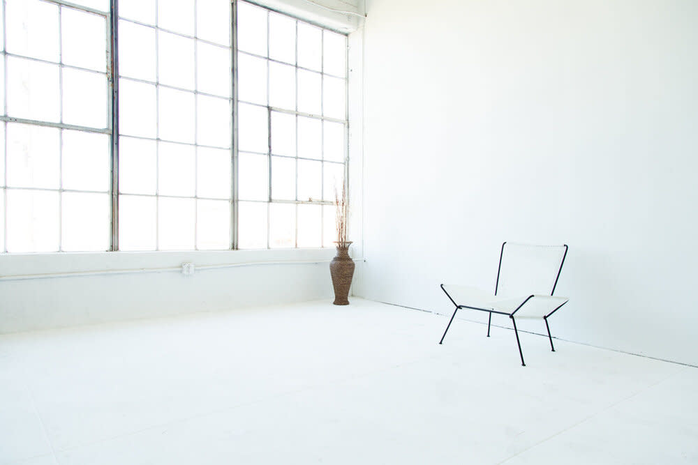 A tall vase with dried branches stands in a sunlit corner of an empty, white-walled room.