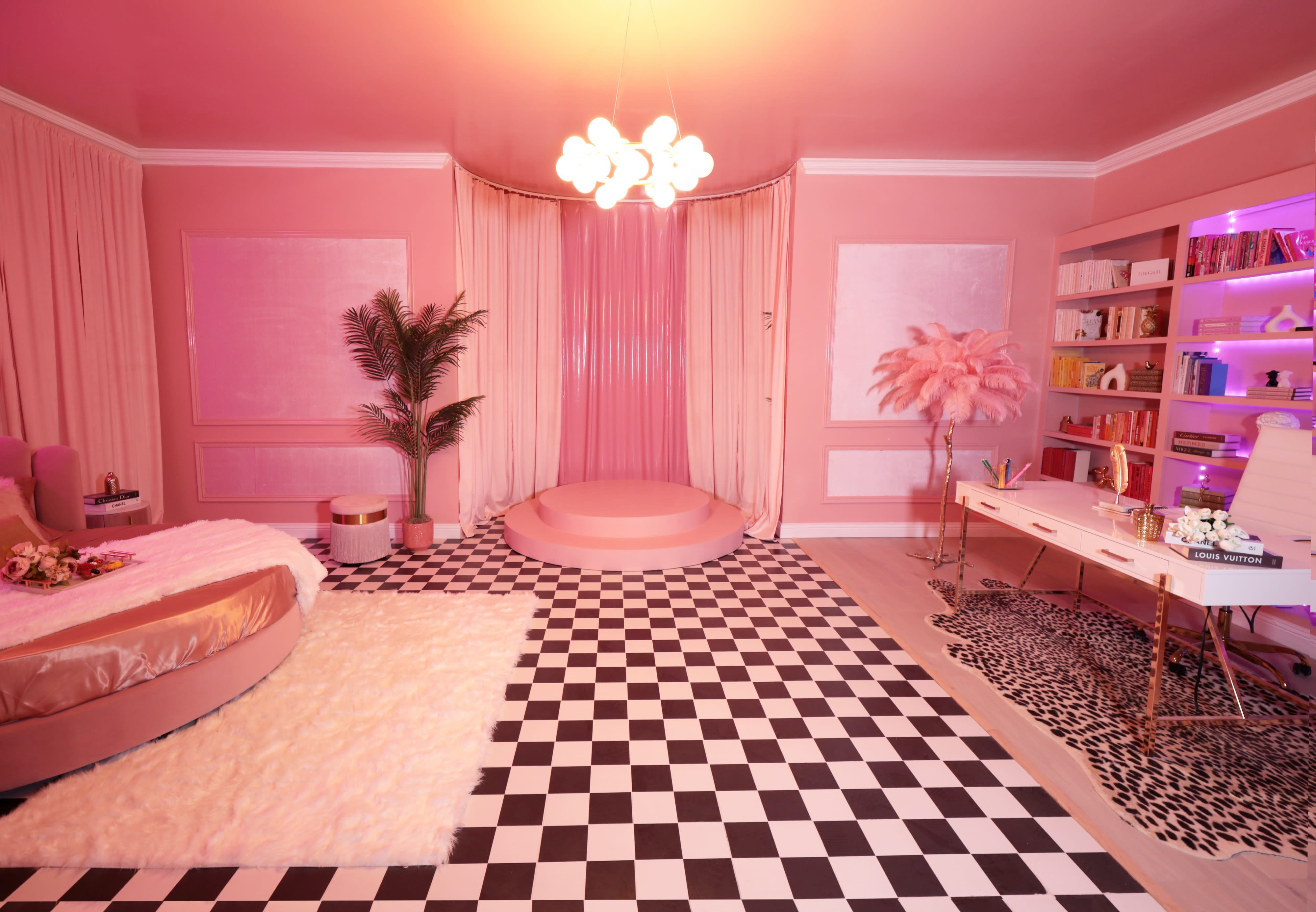 A woman in a pink tulle dress sits elegantly on a plush bed, holding a champagne glass in a vibrant, styled room.