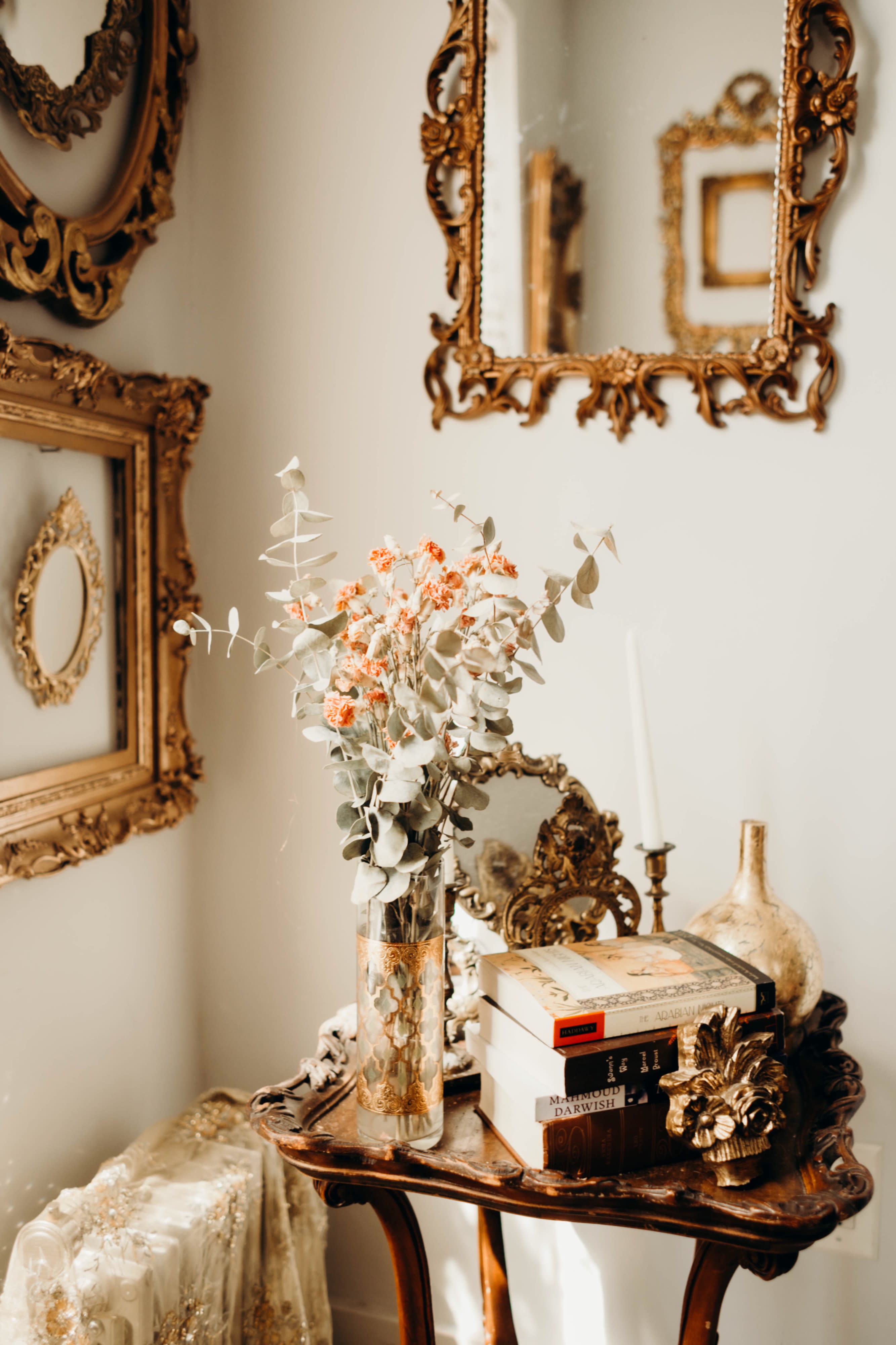 A model poses thoughtfully by a window adorned with ornate gold frames during a photo shoot.