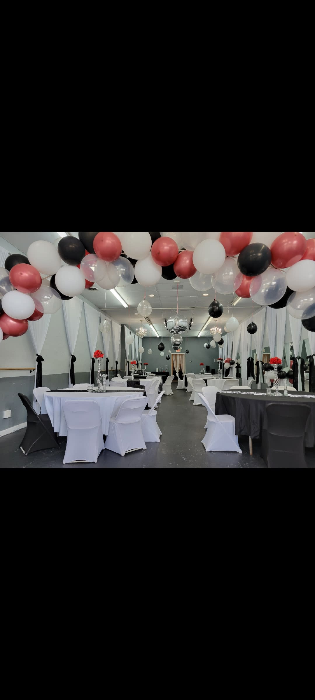 Guests celebrate a first birthday party in a decorated room with tables set for dining and colorful balloons.