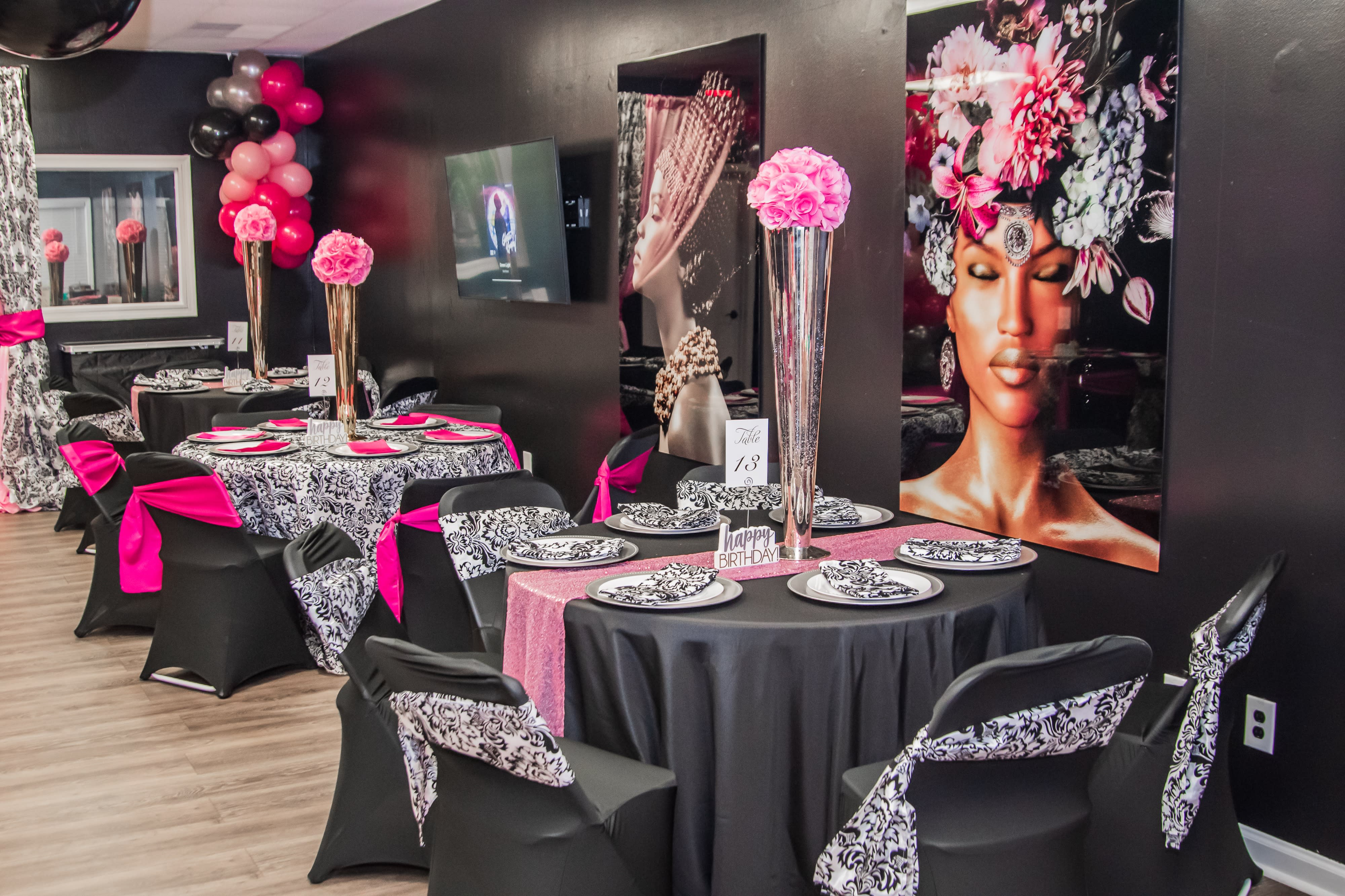A decorated dining table is set for a birthday party, featuring black plates, silverware, and candles as centerpieces.