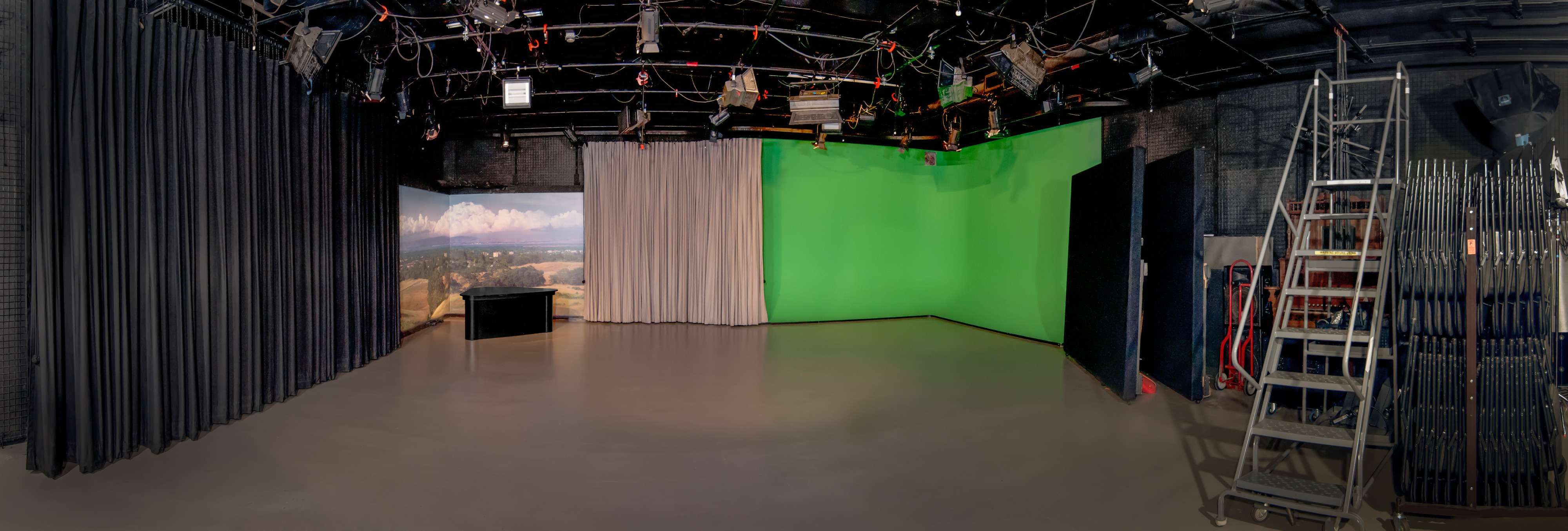 The stage is set with several microphones and tall stools, ready for a performance, illuminated by colorful lights.