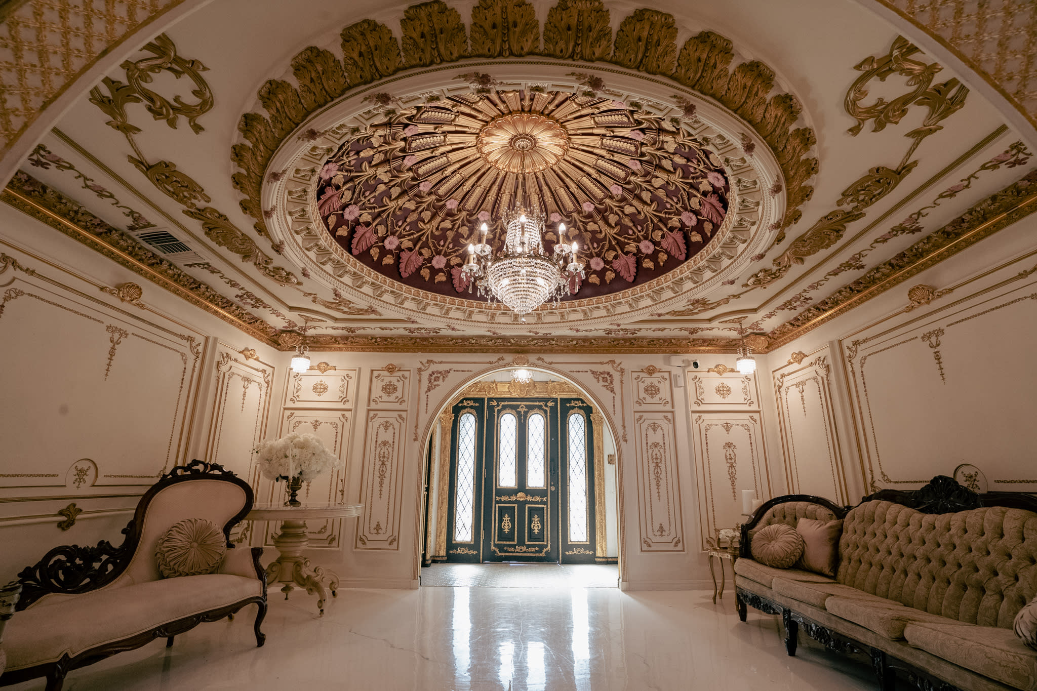 A model dressed in an elaborate historical costume poses gracefully on an ornate couch during a photography workshop.