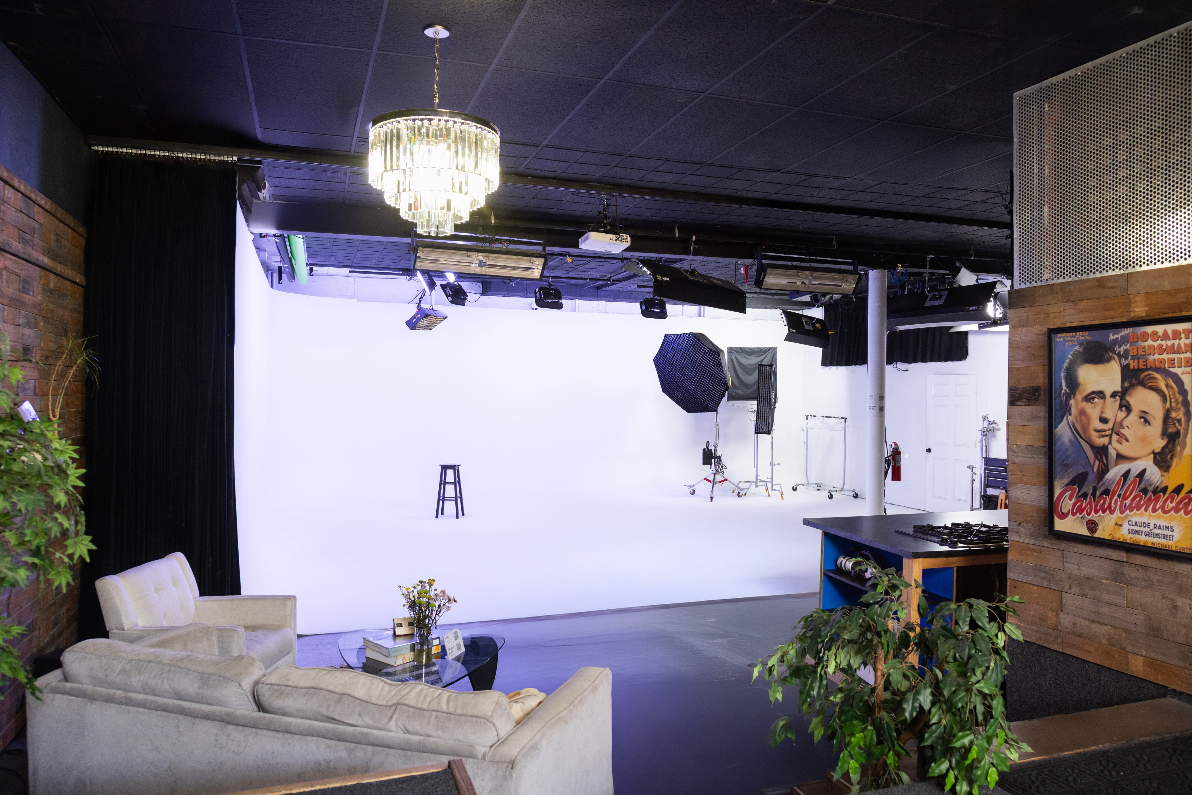 A film crew sets up equipment while an actress prepares for a shoot against a gray backdrop.