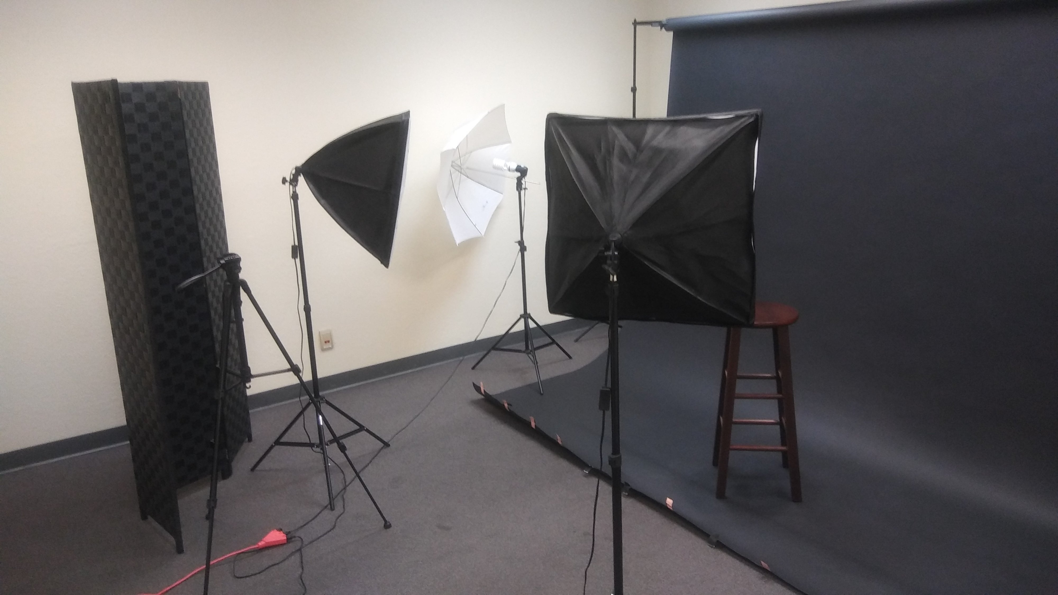 A video shoot features two individuals standing back-to-back in front of a green backdrop.