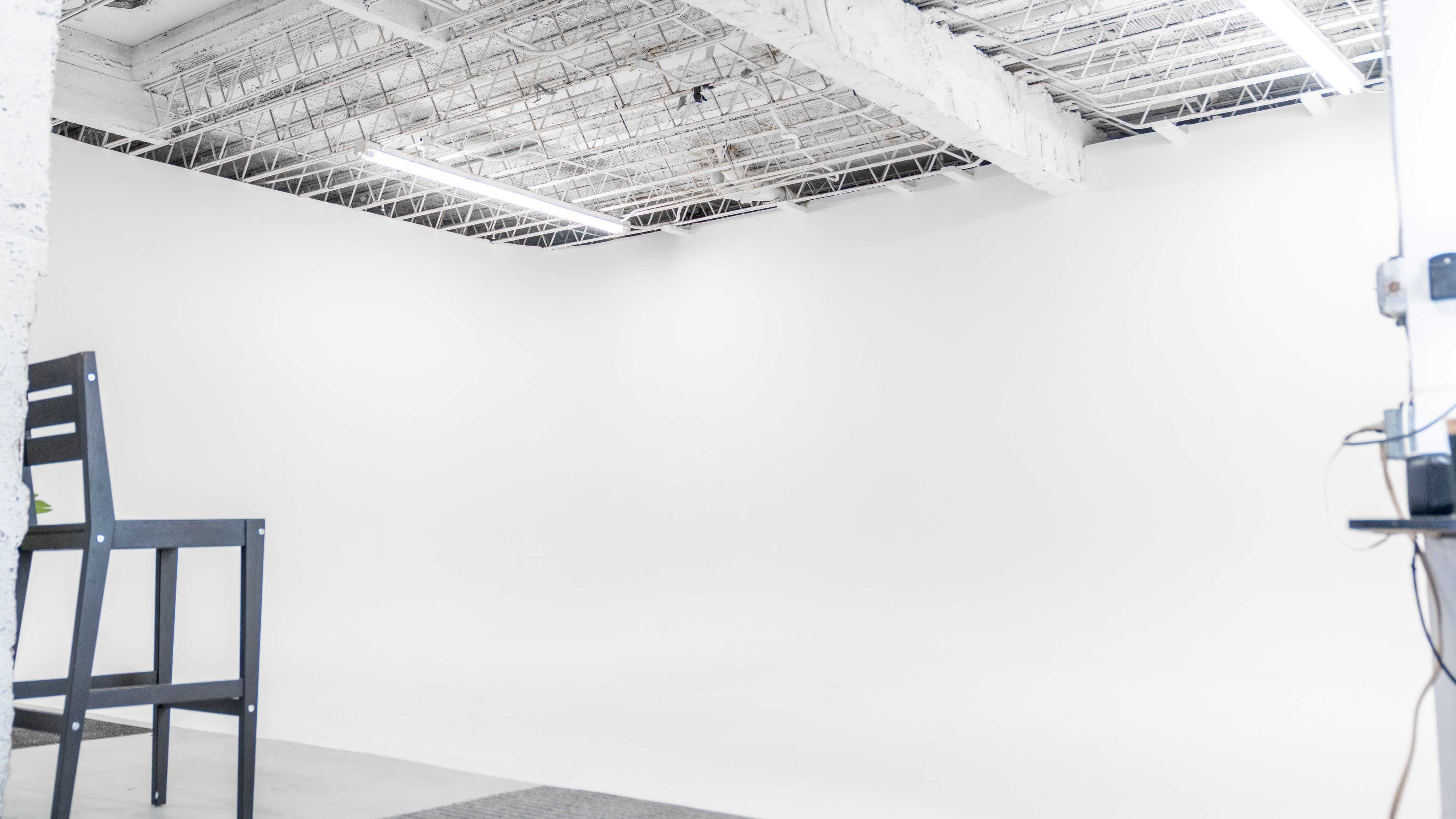 A camera is set up on a tripod, focused on a person standing in a light-filled studio space.