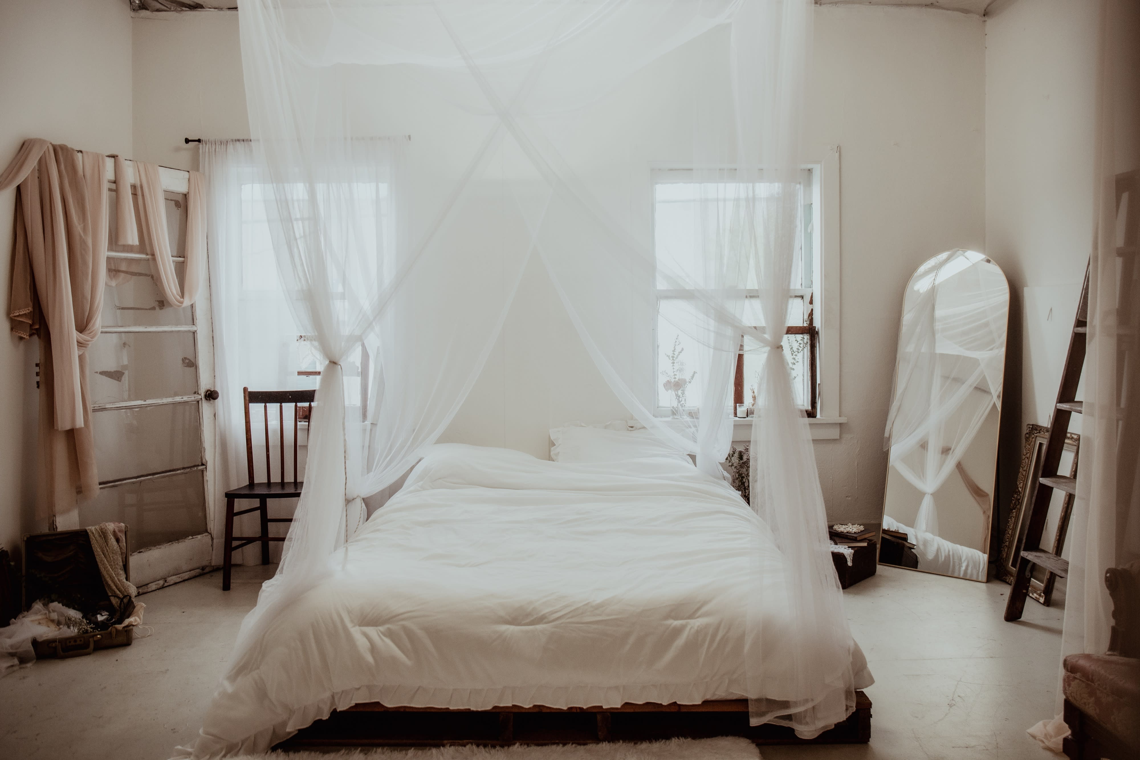 A woman sits on a bed and gazes at her reflection in a large mirror.