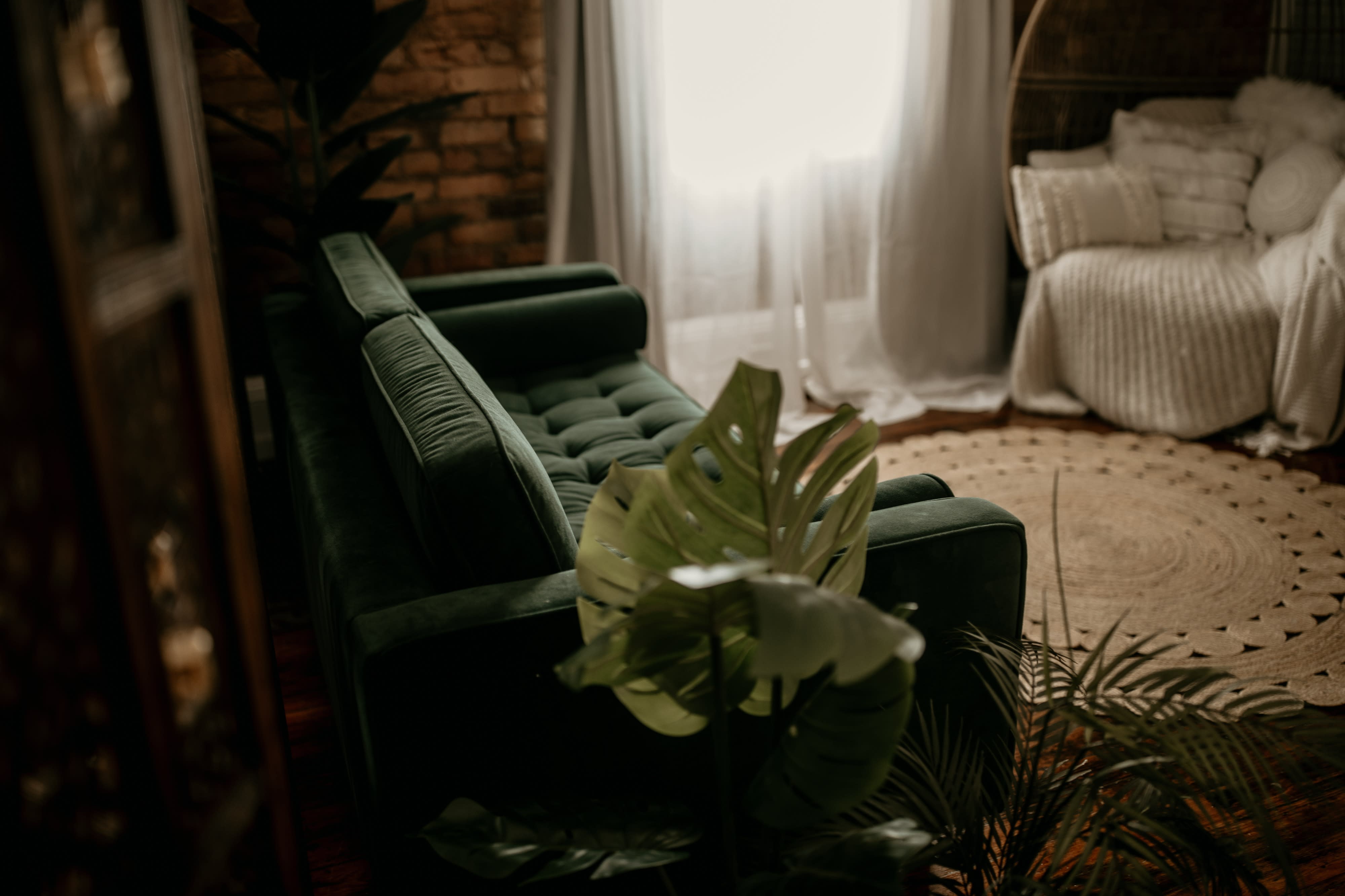 A person sits on a chair, gazing upward while positioned near a window with sheer curtains.