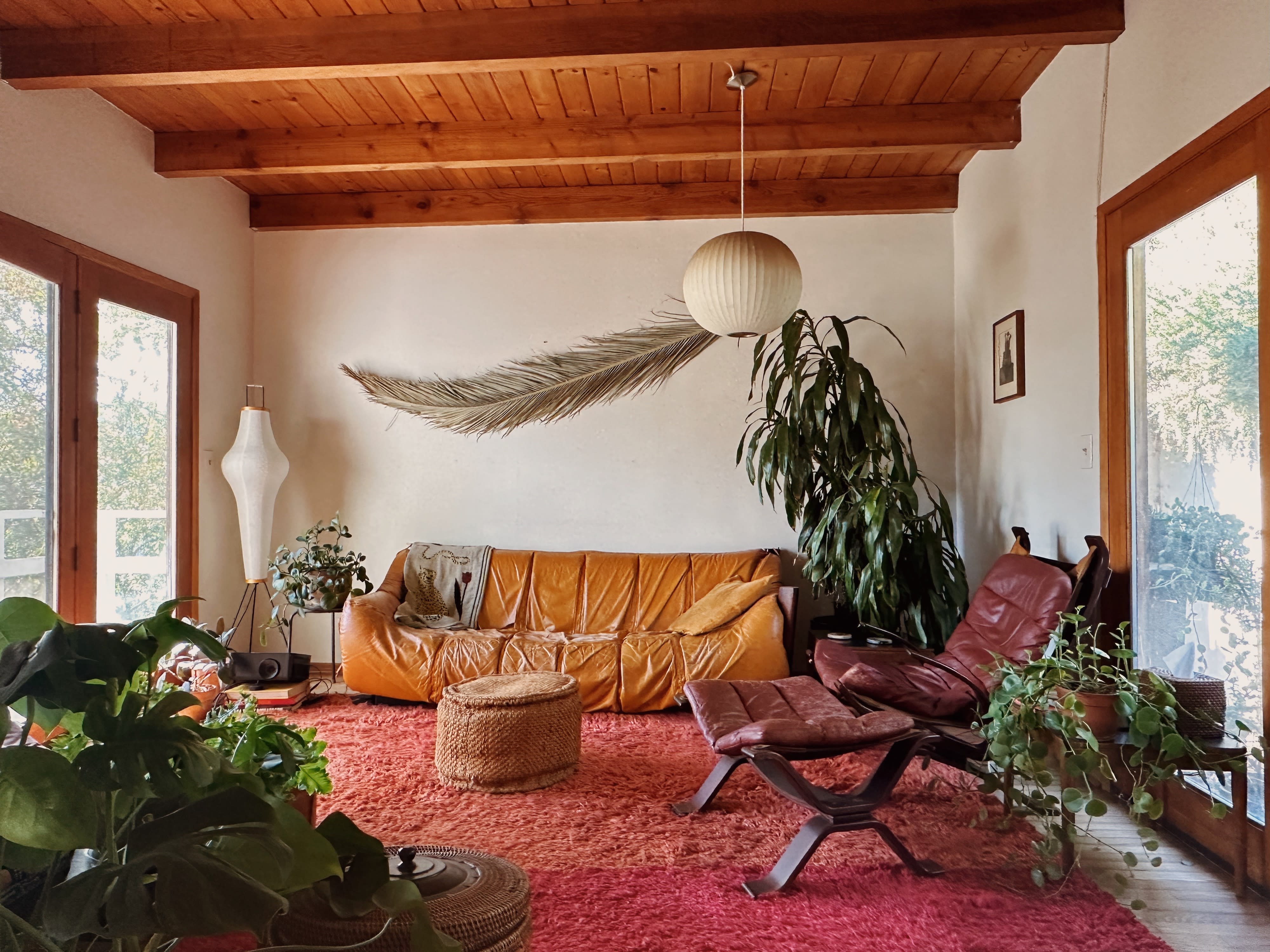 A video shoot is taking place in a cozy living room featuring an orange sofa surrounded by shelves filled with various decorative objects and books.