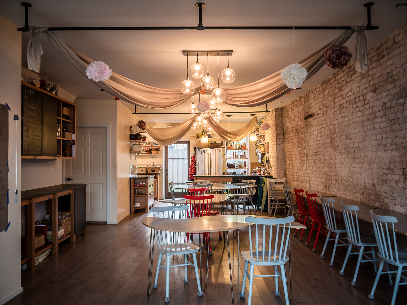 The spacious venue is set up for a baby shower, featuring decorated tables and colorful chairs along with draped fabric overhead.